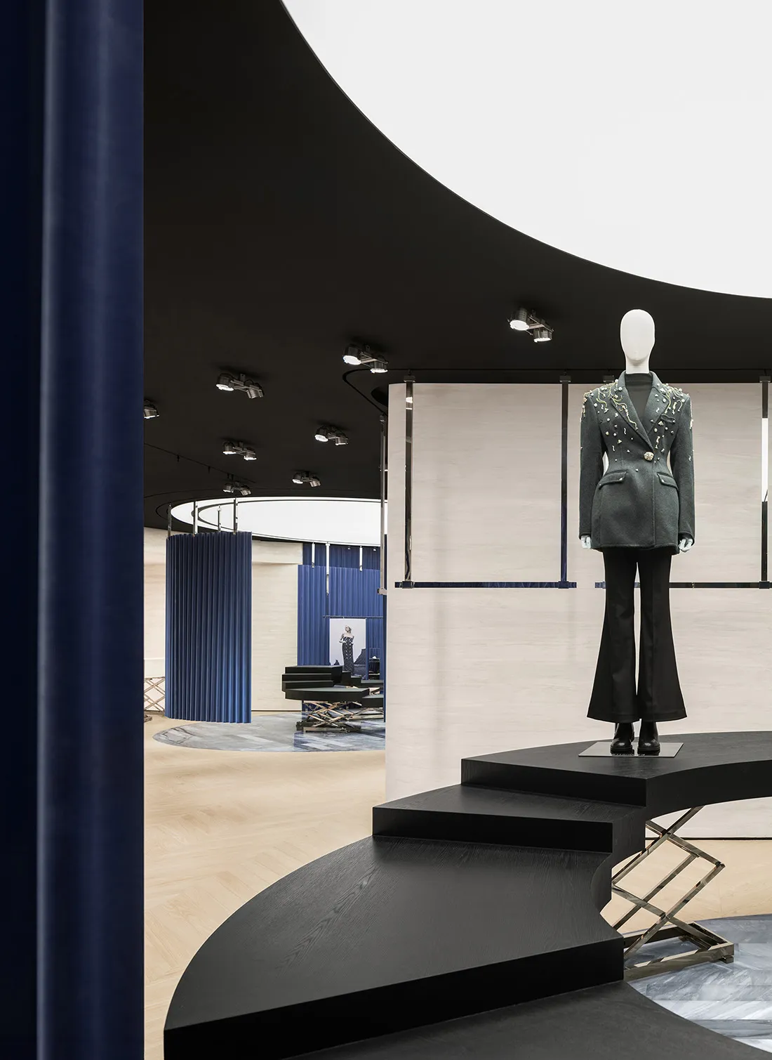 A modern retail space featuring a fashion exhibit with a mannequin wearing a stylish jacket and pants on a curved black platf