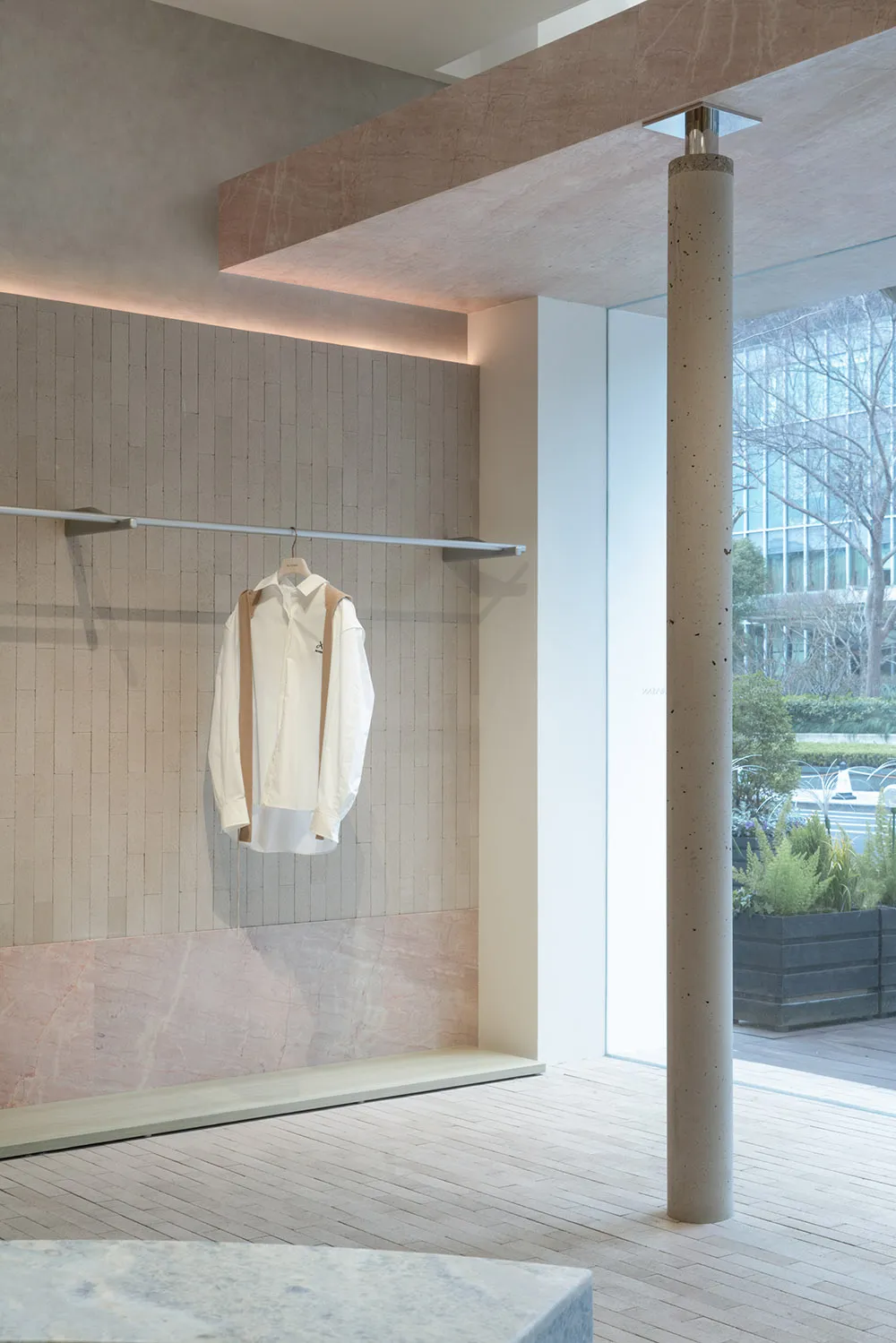 現代服飾店展示,採用淺色混凝土牆面,單件白色襯衫懸掛於橫桿上。