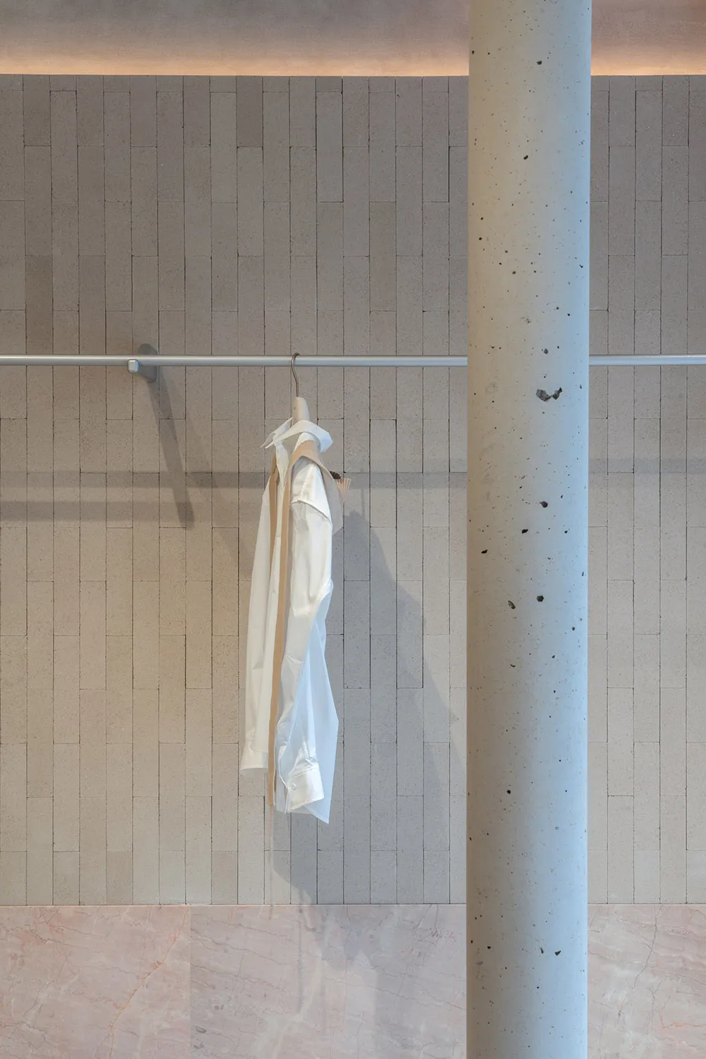 Clothing hanger with white fabric hanging on a wall-mounted horizontal bar in a concrete interior space.