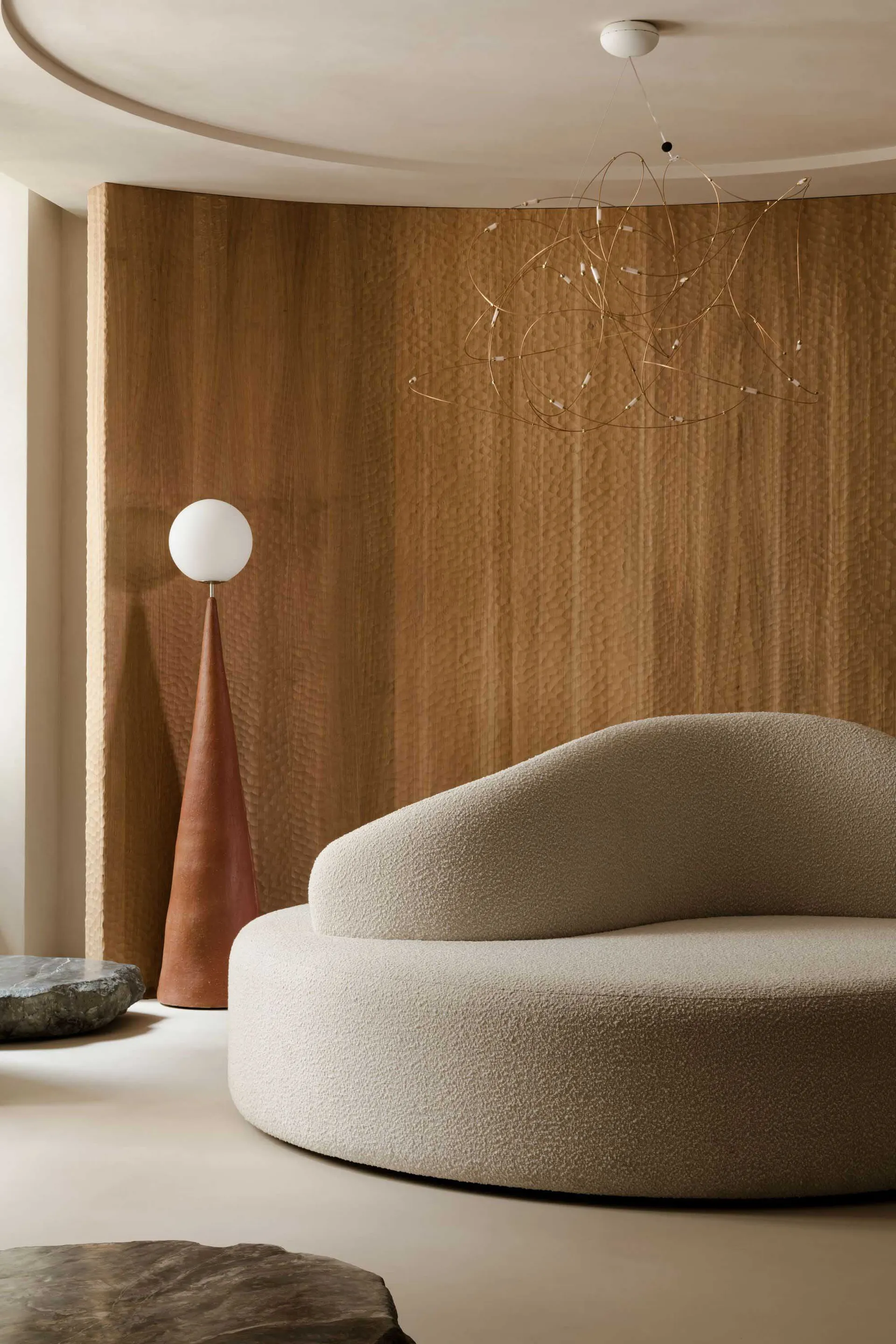 A modern circle sofa in textured fabric against a wooden wall, with a unique hanging light fixture.