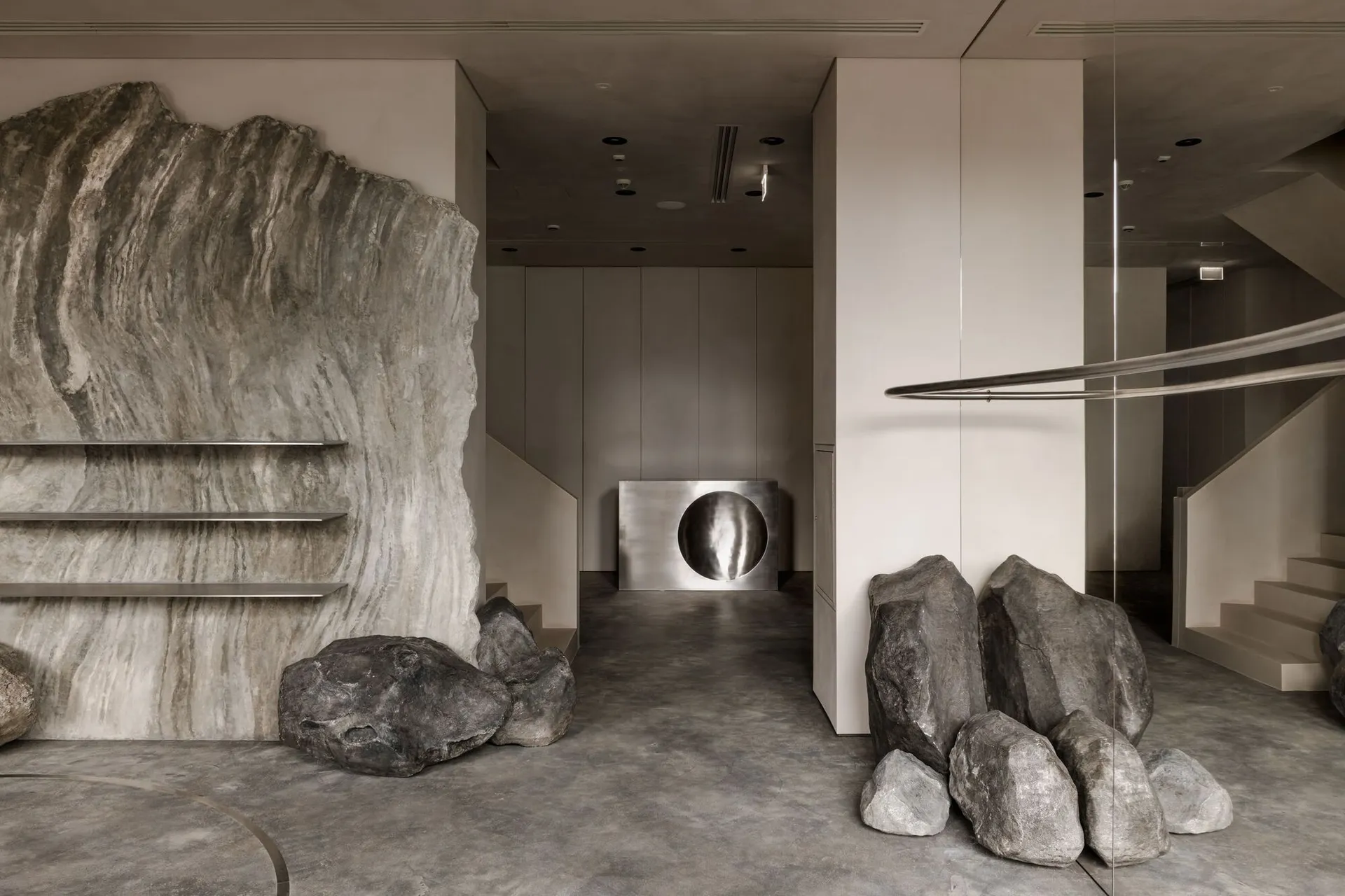 A modern lobby with concrete walls and large rocks, featuring a metal column with a circular opening.