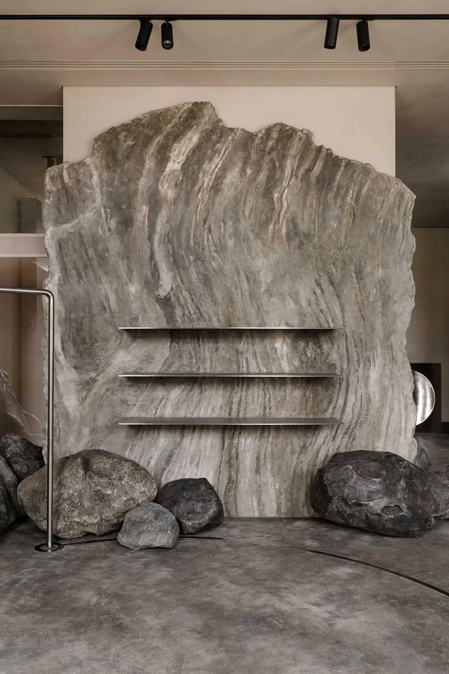 A modern interior design featuring a large, textured marble wall with minimalist shelves and decorative rocks.