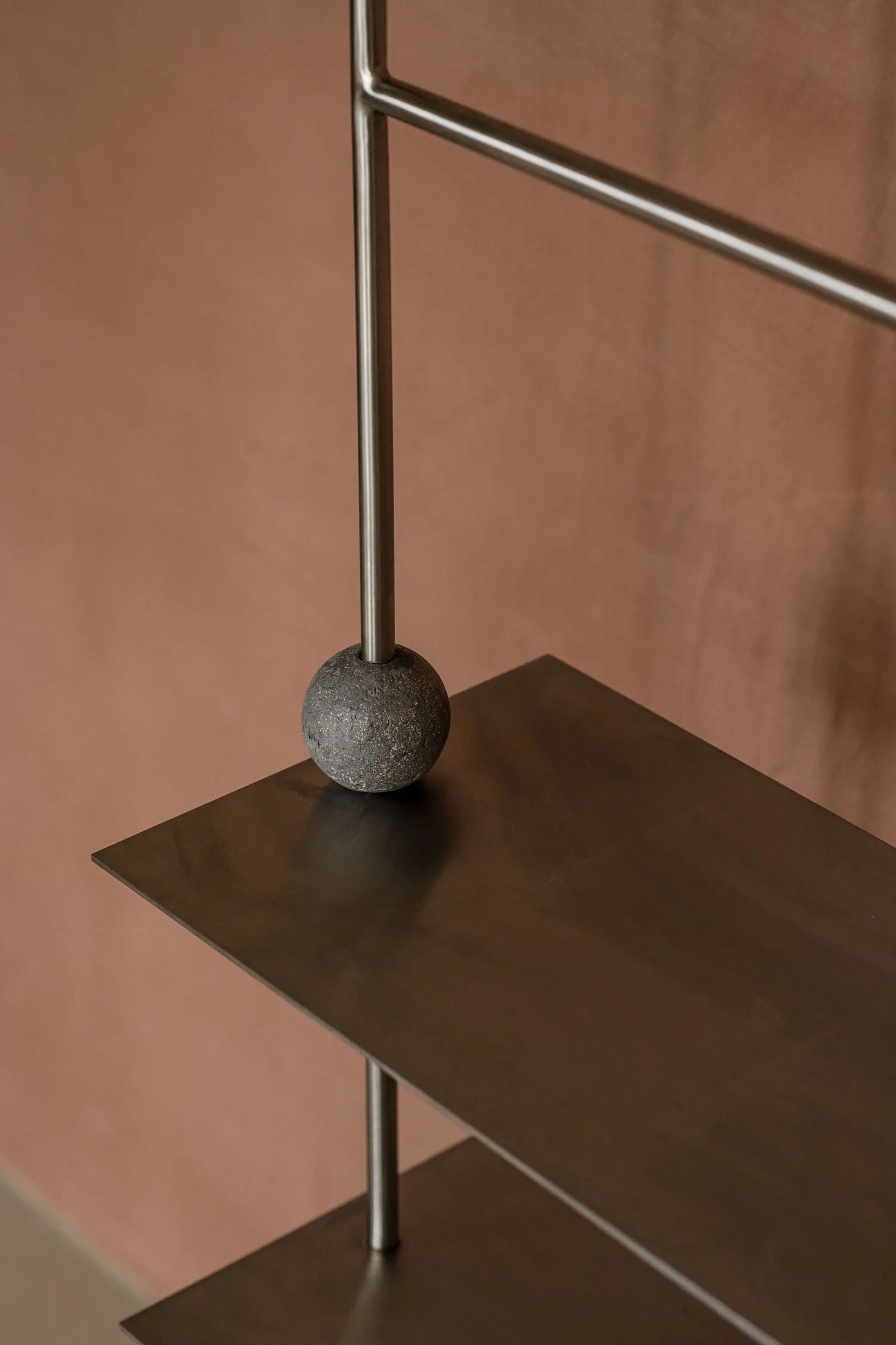 Modern metallic shelving system with geometric design and stone sphere on top.