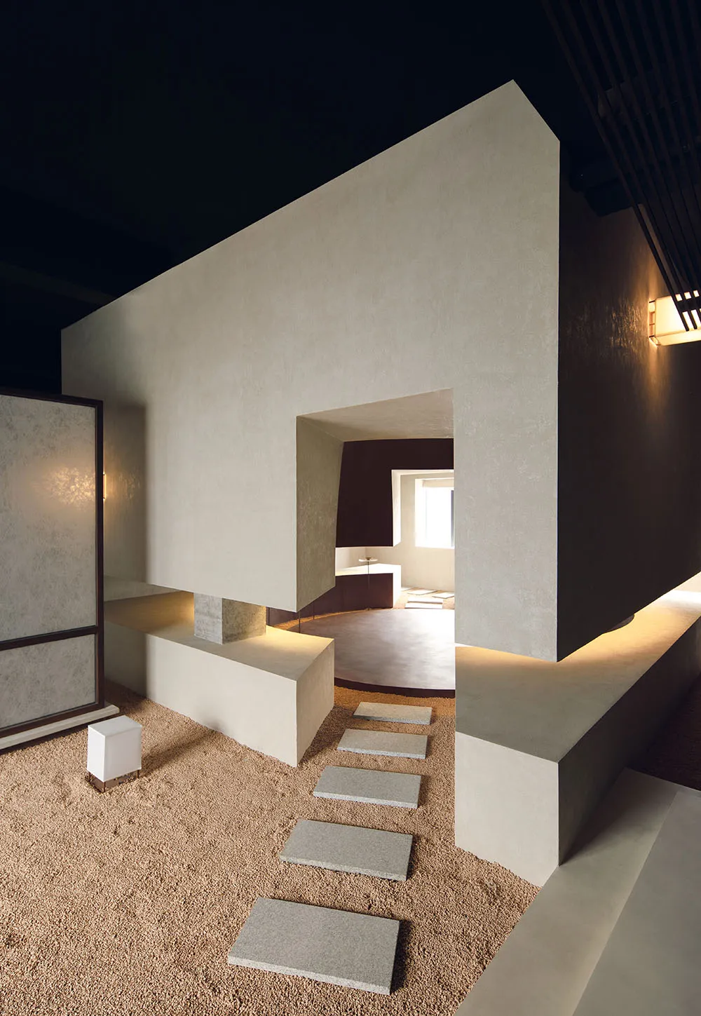 A minimalist living room with concrete walls and floor, a white lighting fixture, and white steps.
