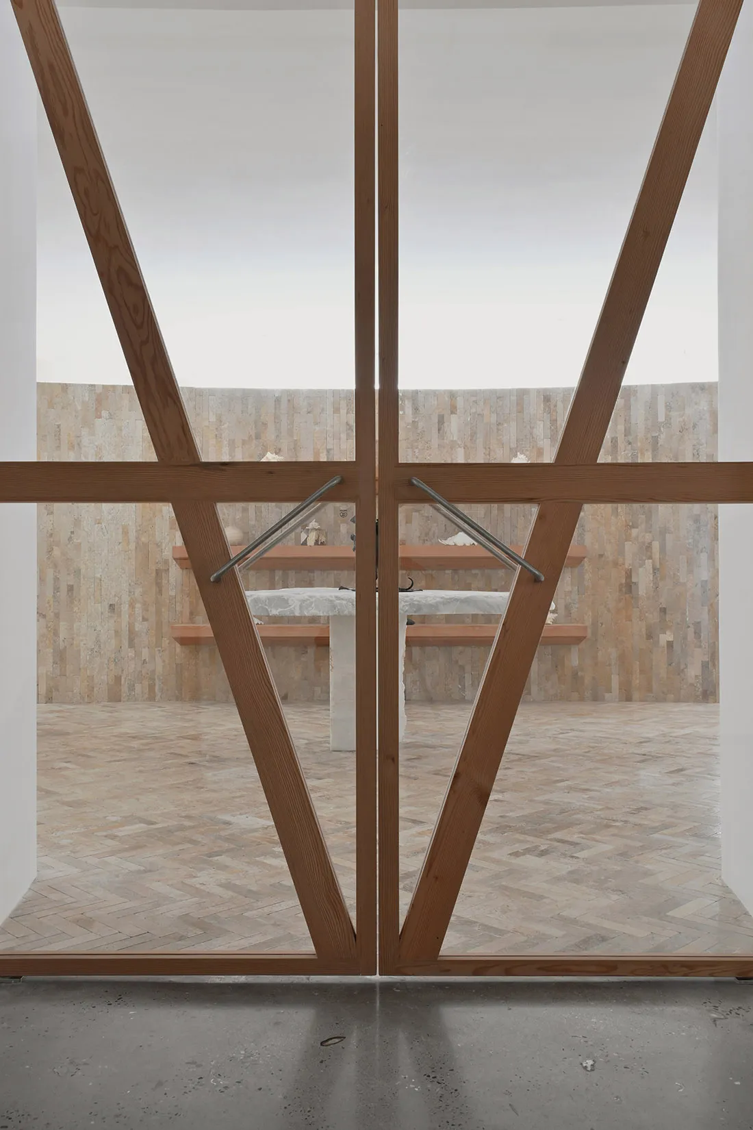 A modern interior with wooden elements, including a table and benches in front of a wall of stone tiles.