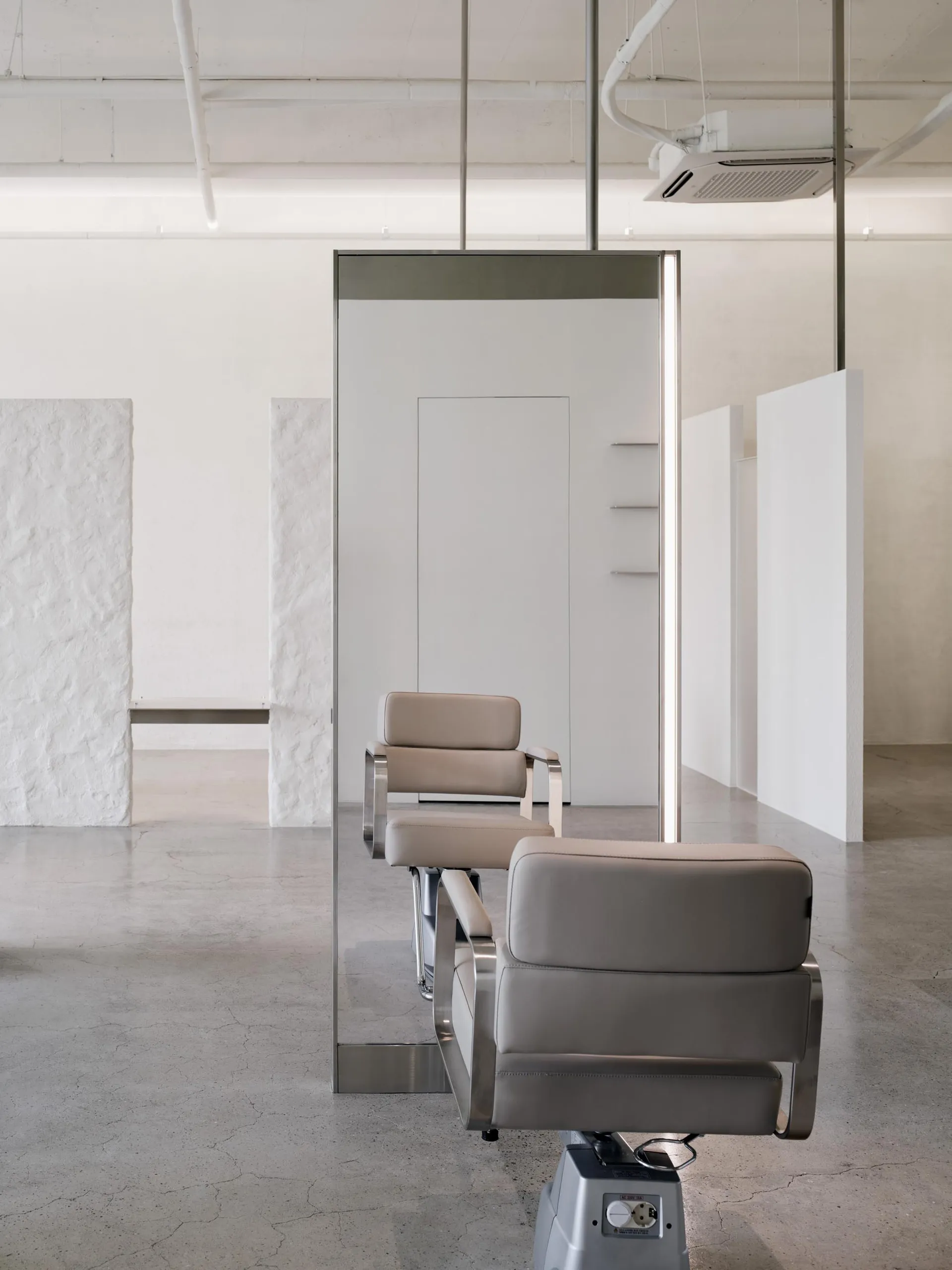 Modern spa interior with minimalist design featuring sleek, neutral-colored leather furniture and a large wall mirror.