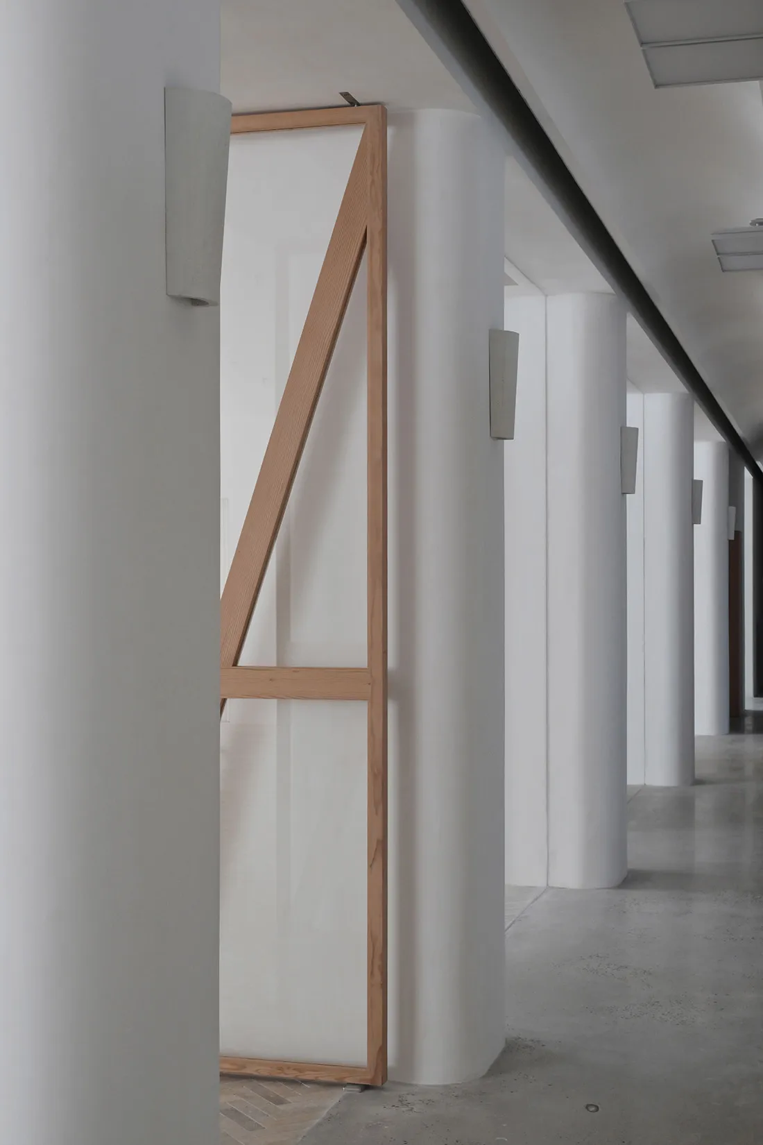 A minimalist corridor with concrete walls, white columns, and a wooden frame