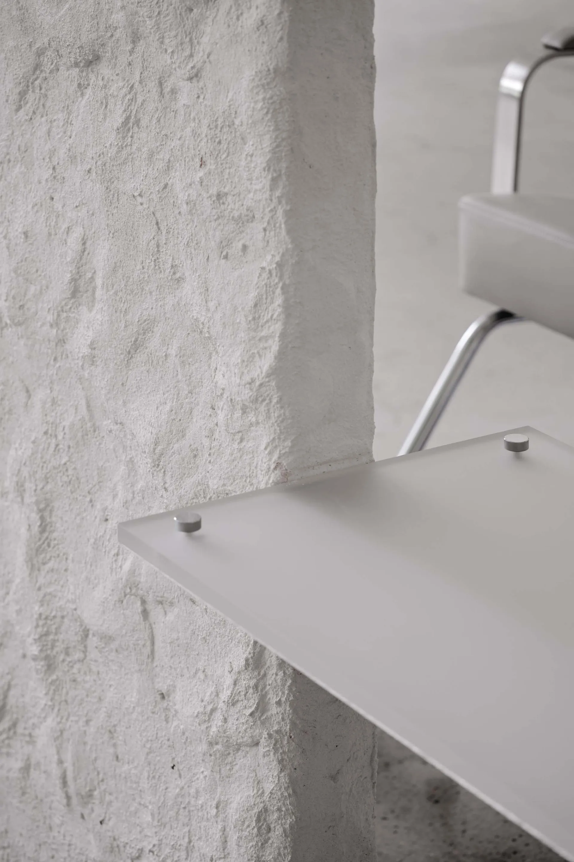 Modern minimalist floating shelf made of clear glass with metal hardware against a textured concrete wall