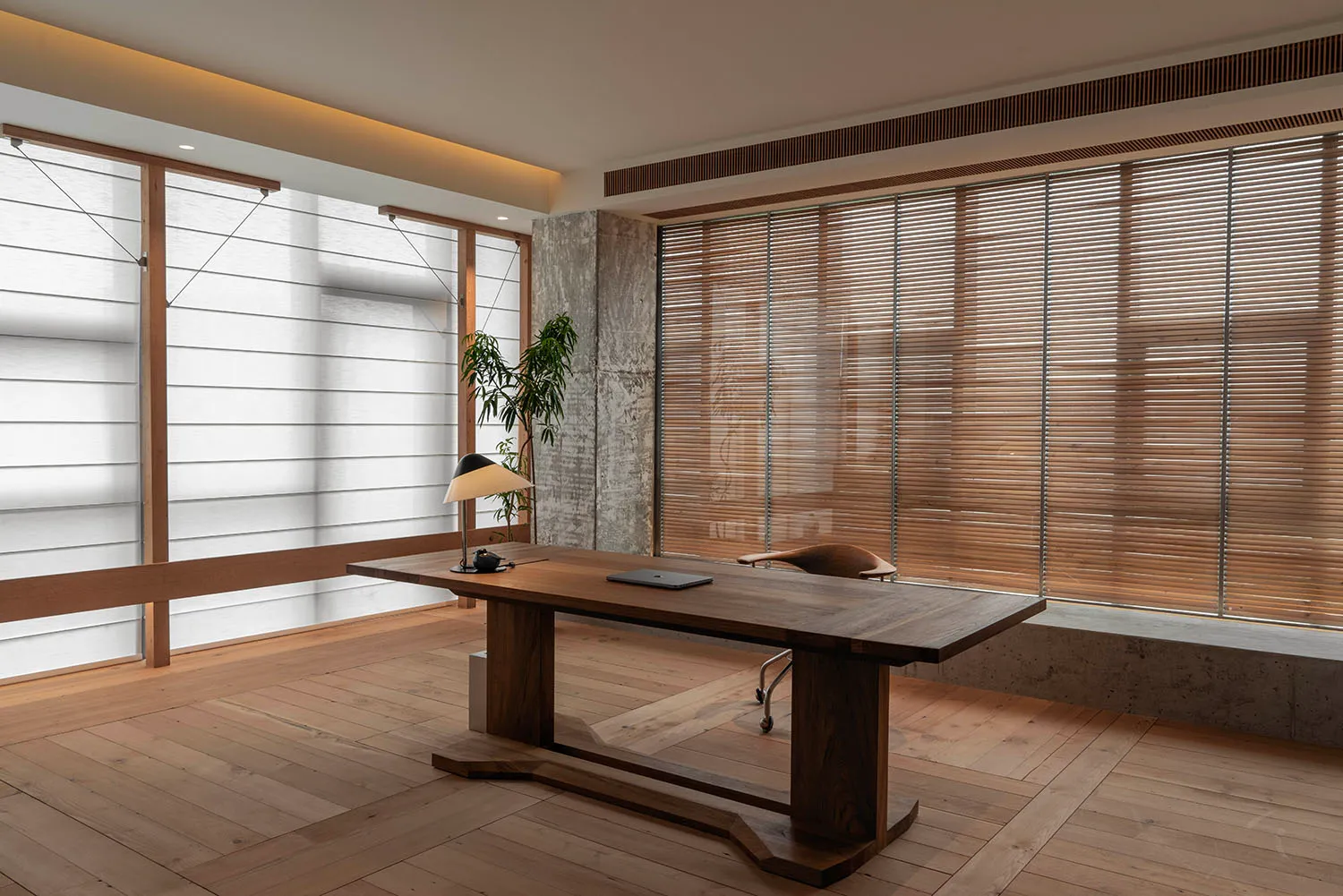 Modern minimalist office space featuring a wooden desk, desk lamp, and wooden floor, with concrete walls and light wooden bli