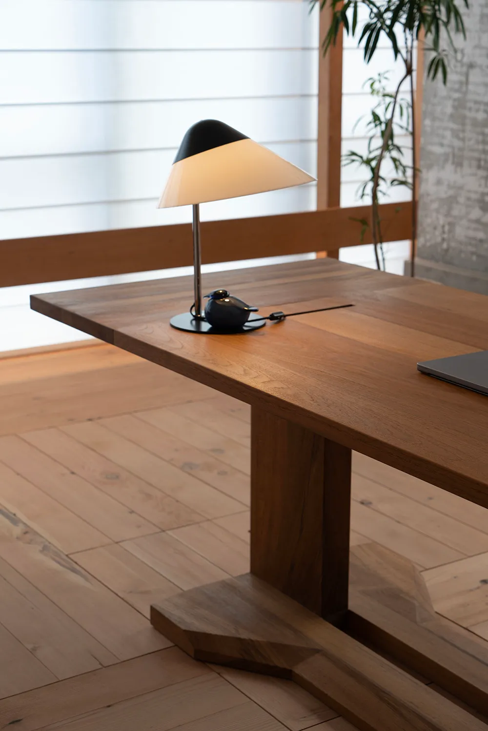A modern minimalist desk made of wood with a white table lamp on it.