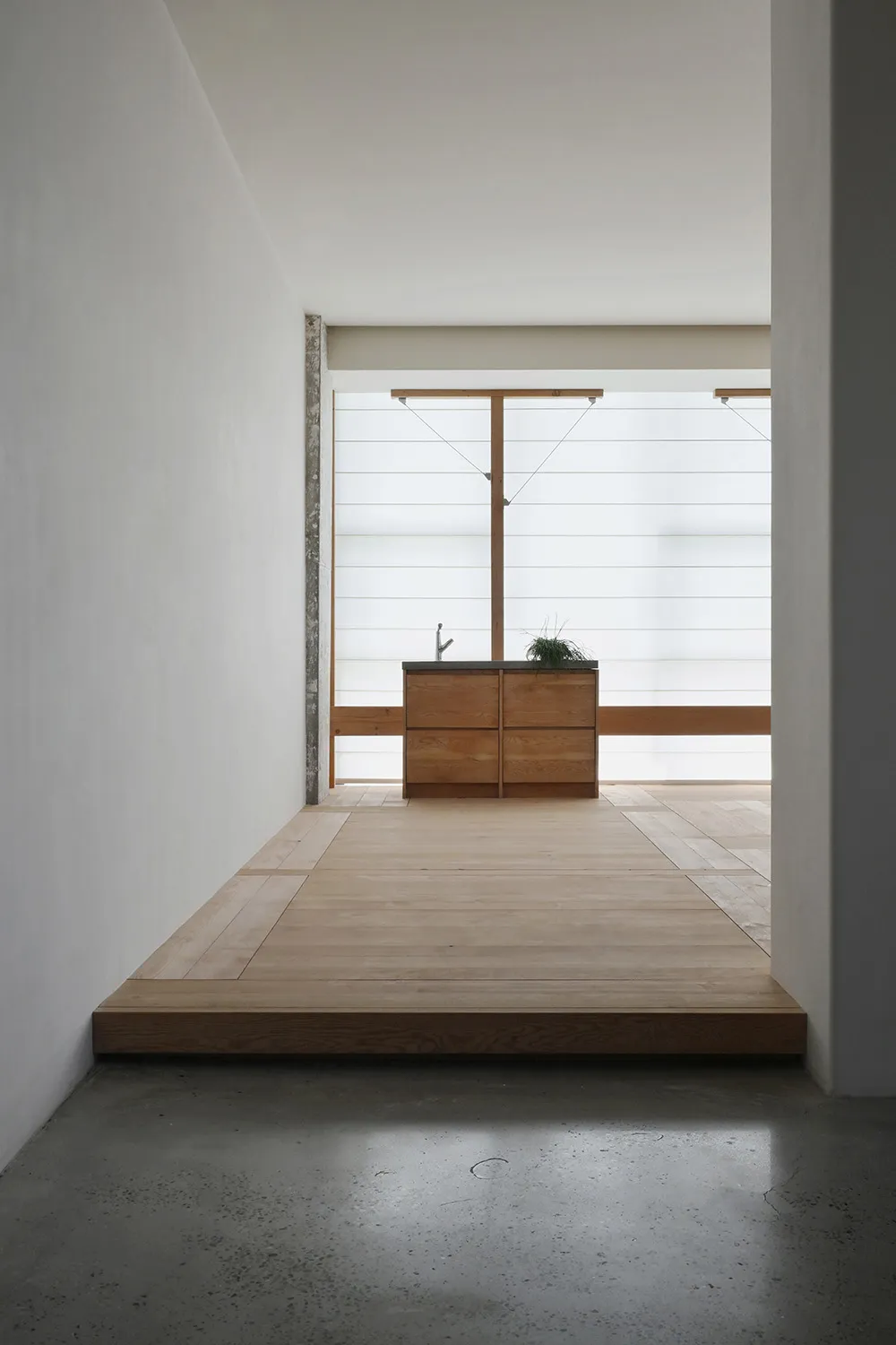 Minimalist residential kitchen featuring wooden flooring and a wooden cabinet with a sink and a plant.
