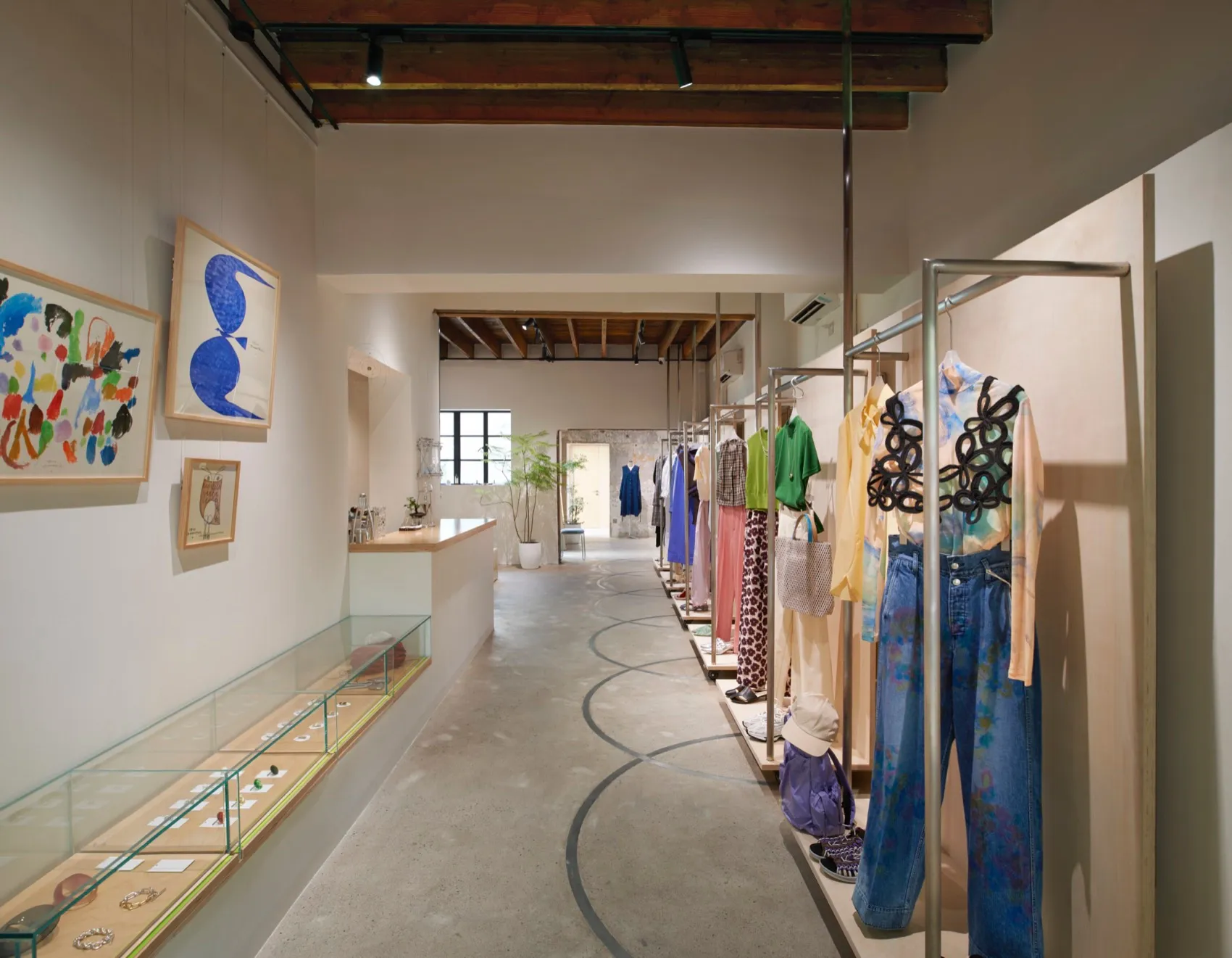 A clothing store with modern interior design, featuring colorful clothing on racks and abstract art displayed on the walls.
