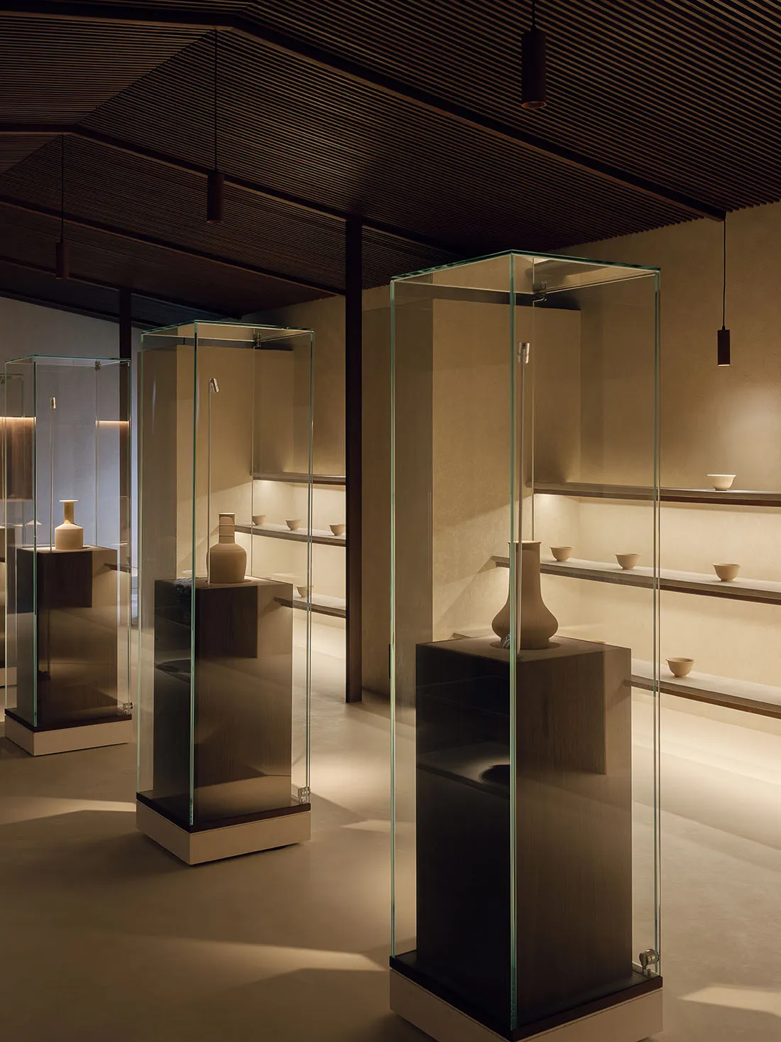 Modern interior design exhibition with glass cases showcasing various ceramic vases and bowls on wooden pedestals.