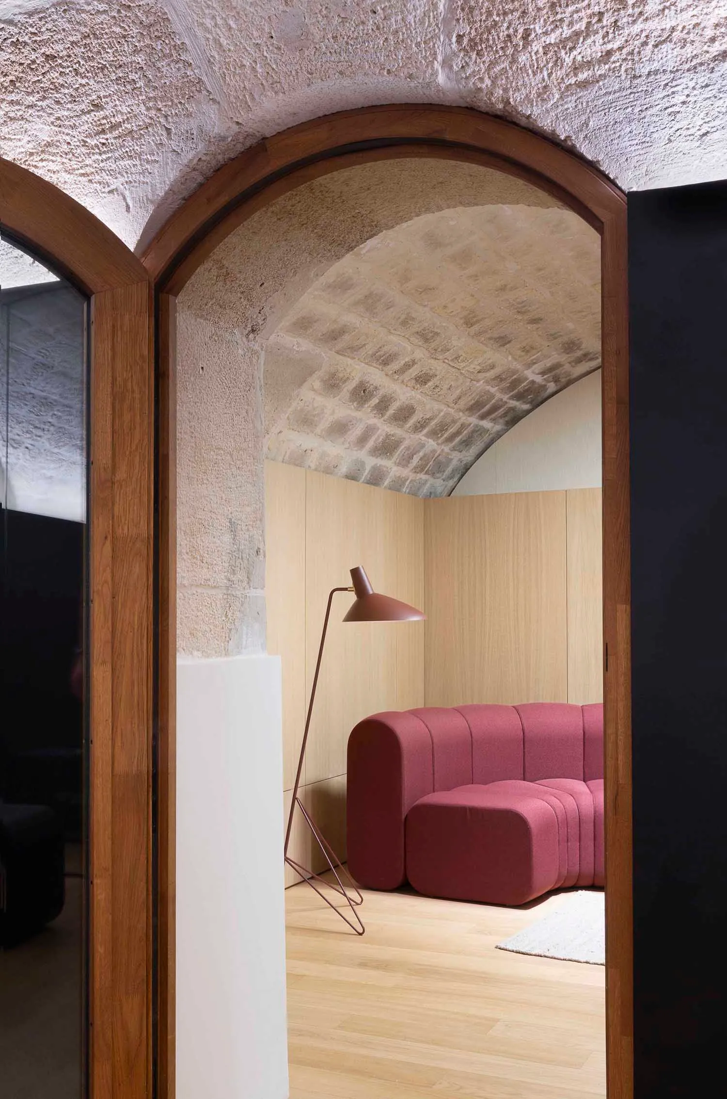 A room with an arched doorway featuring a textured concrete wall, wooden flooring, and a modern sofa in a geometric, minimali