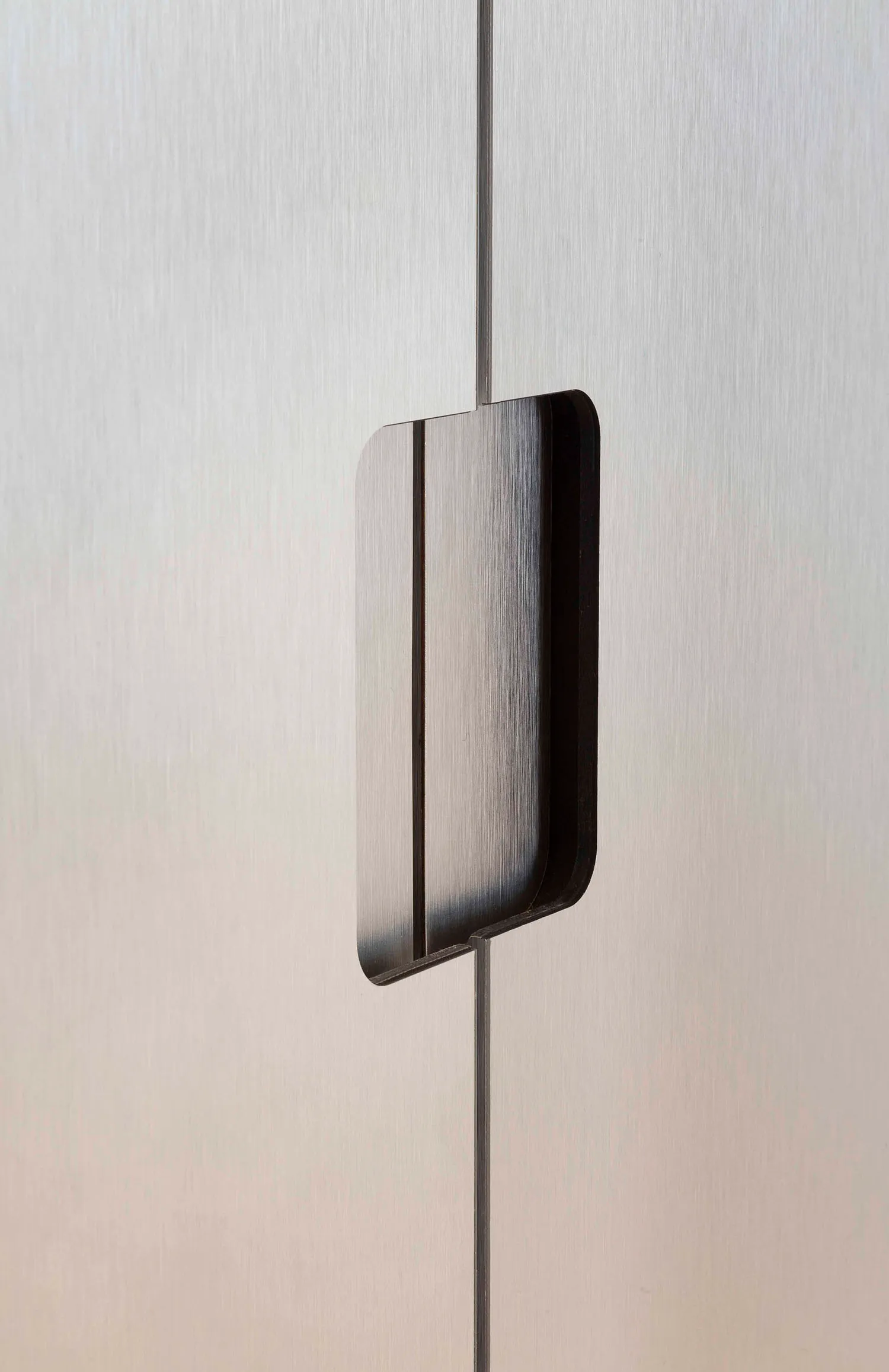 A minimalist metal handle mounted on a brushed aluminum surface.