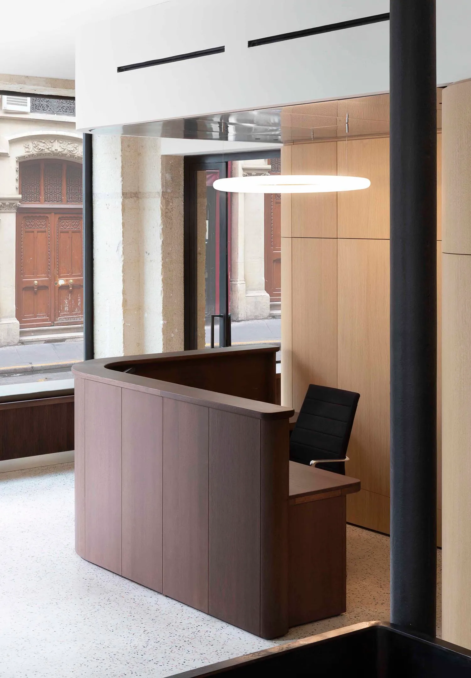 A spacious, minimalistic interior design featuring a wooden reception desk and a sleek, modern office space.