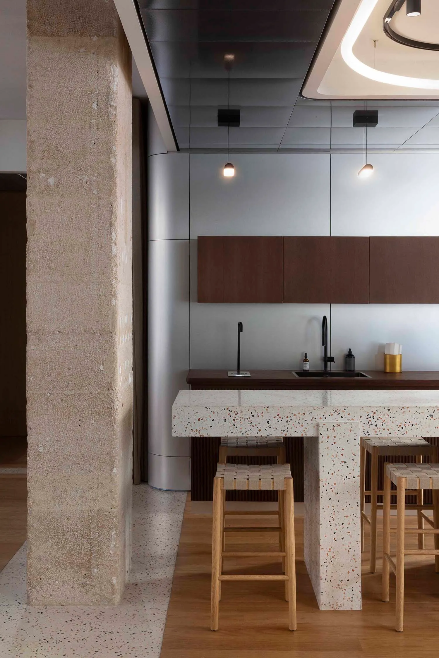 Modern kitchen featuring a marble and terrazzo counter with wooden stools.