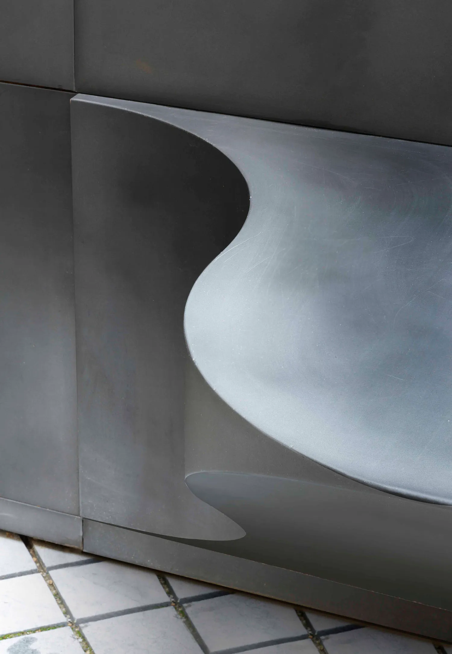 A sleek, modern metal bench sitting on a tiled floor.