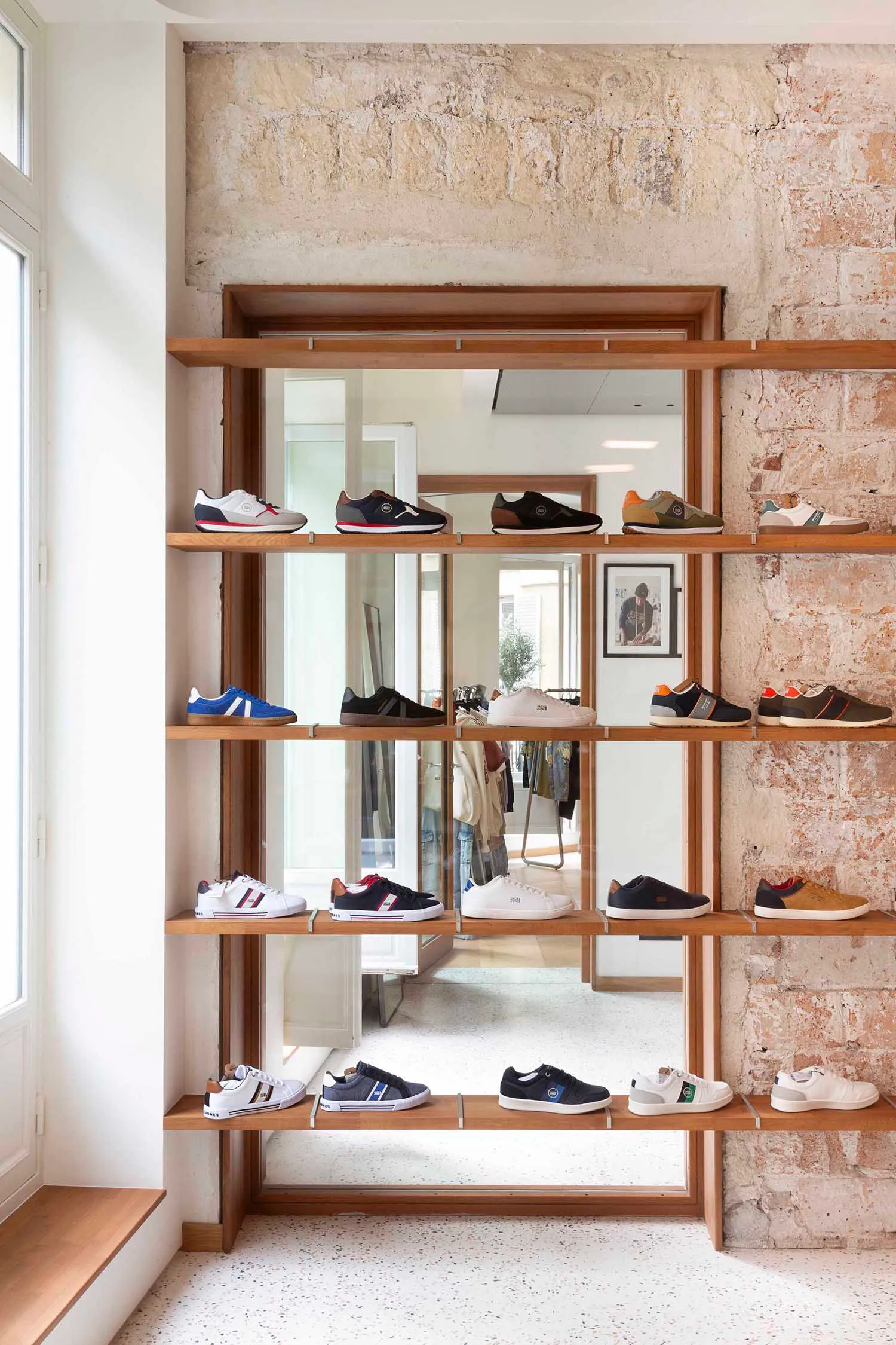Modern shoe shop display featuring a variety of sneakers on wooden shelves against a rough-hewn stone wall with a terrazzo fl