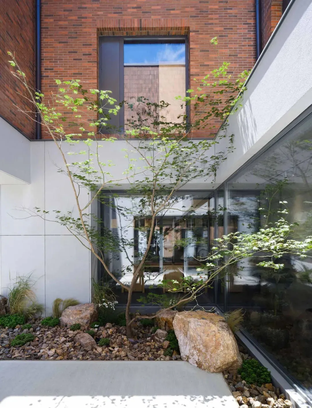 Modern residential entry with brick walls, glass windows, and rock landscaping.