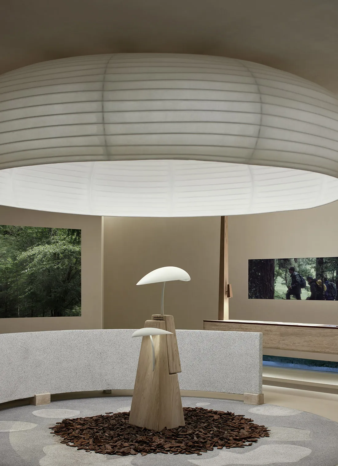 A minimalist lamp with a wooden base and a concrete counter is surrounded by a white fabric ceiling and a forest view.