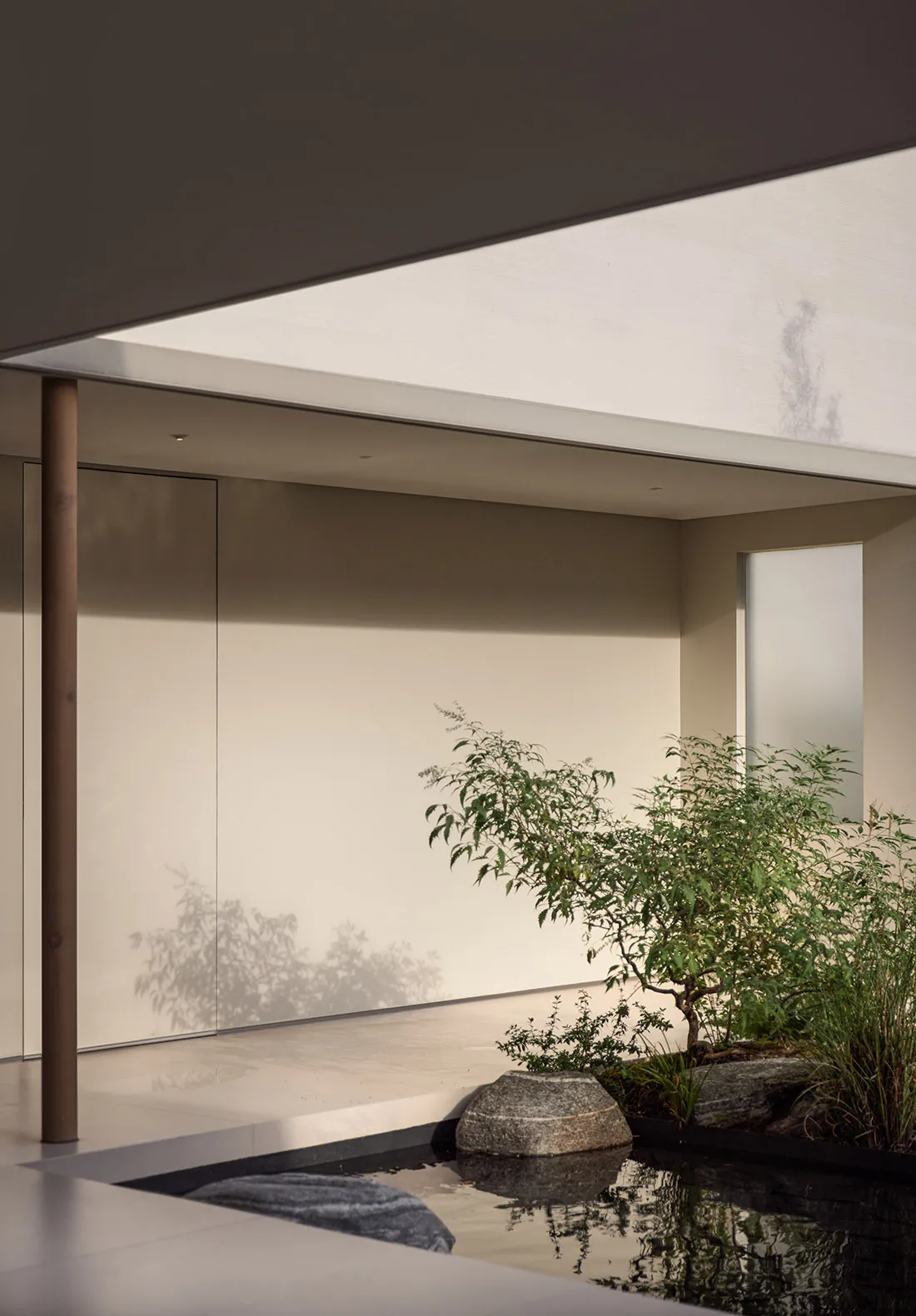 Modern interior with minimalist design, concrete floor, glass walls, and Japanese garden elements.