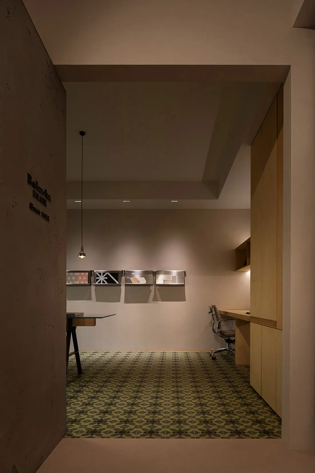 A minimalist office space featuring concrete walls and flooring, illuminated by warm lighting.
