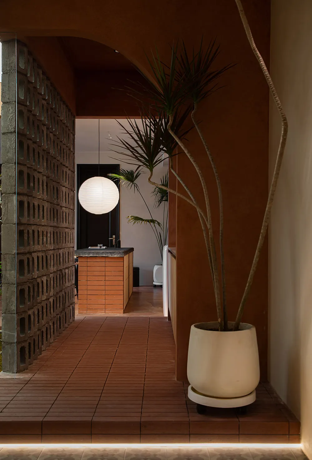 Modern entryway featuring brick walls, concrete arch, potted plants, and a spherical light fixture.