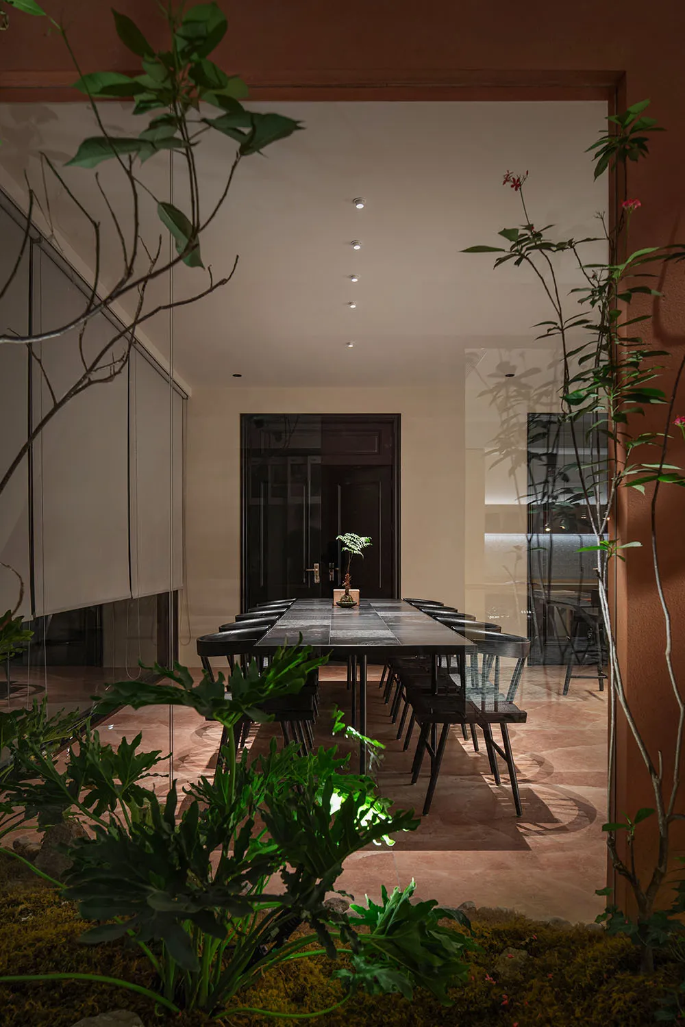 A modern dining room featuring a long rectangular table adorned with a small plant, surrounded by wooden chairs, set within a