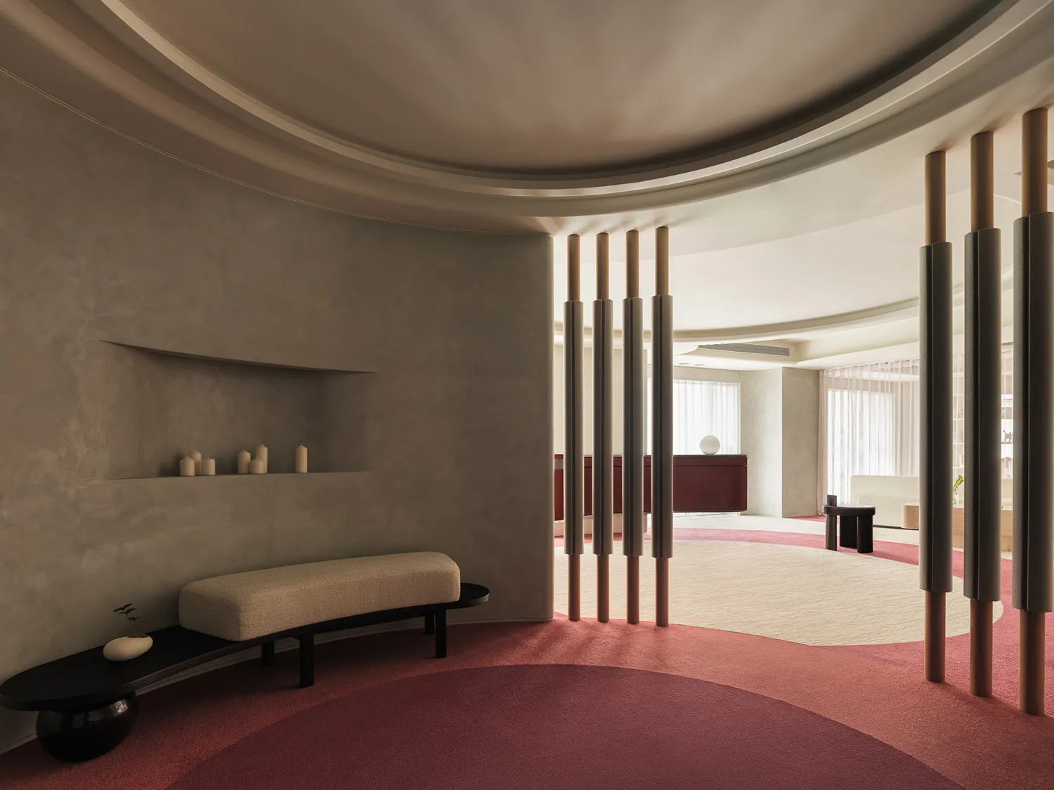 Modern living room with concrete walls, wooden pillars, and red carpet, featuring minimalist furniture and large windows with
