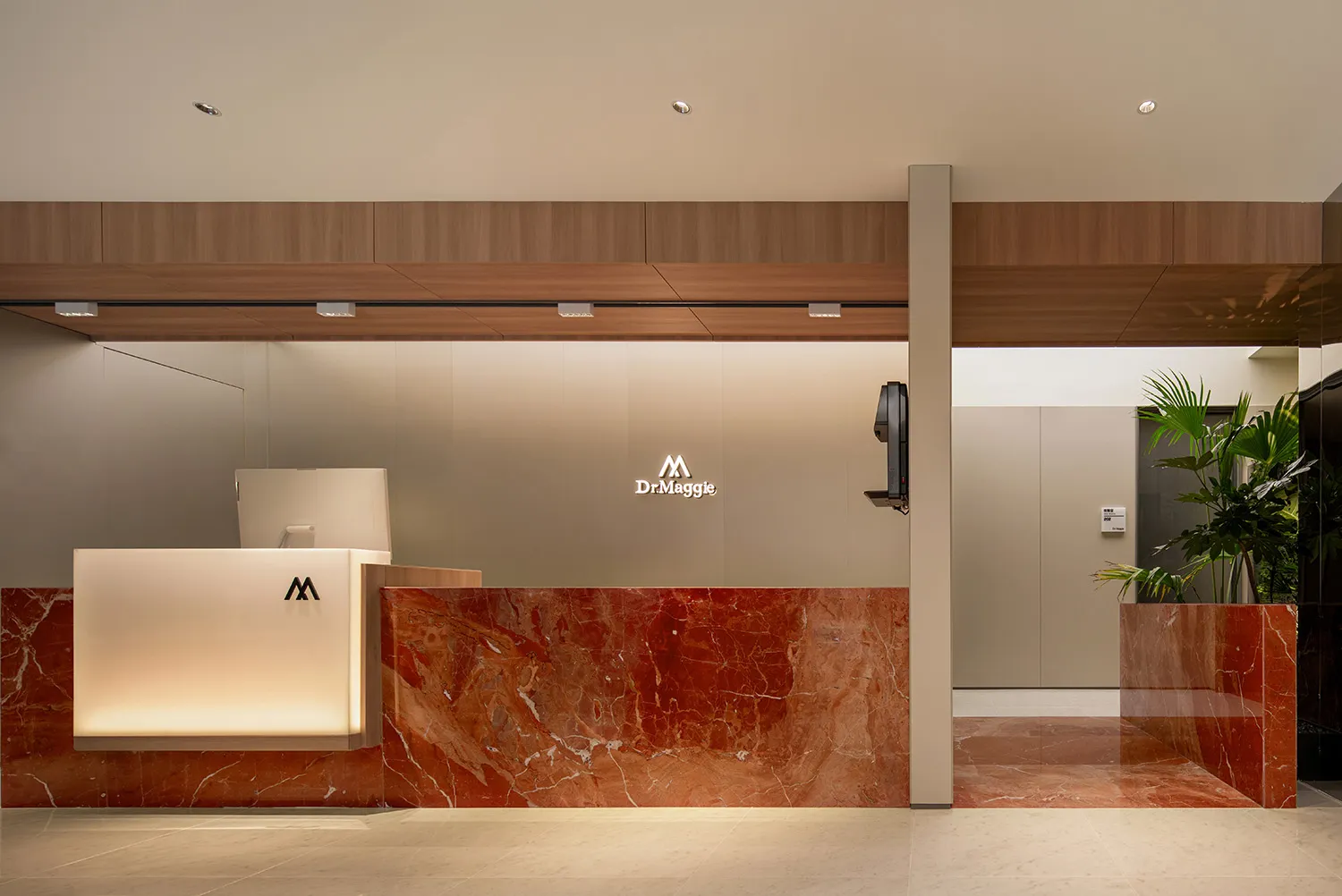 An image of a modern lobby featuring a reception desk made of red marble with a white illuminated counter and a sleek design.