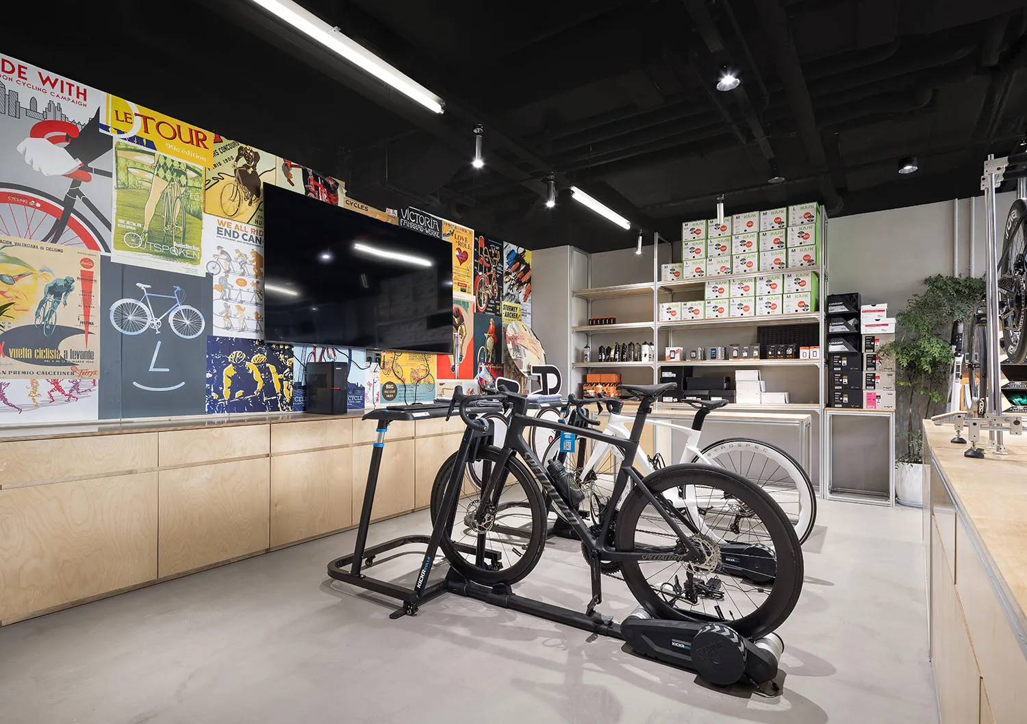A modern bike shop with metal and wood elements, featuring a large screen TV and several bicycles on stands.