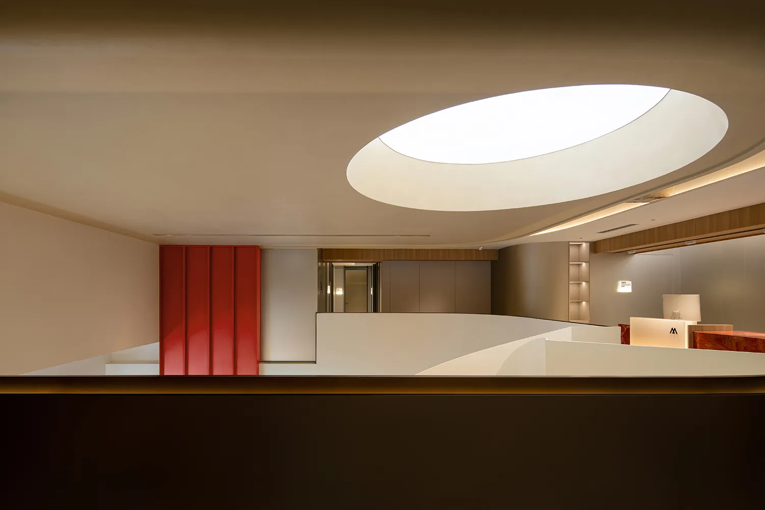 Modern office space with a red geometric feature on the wall, illuminated by natural light from a large circular skylight.