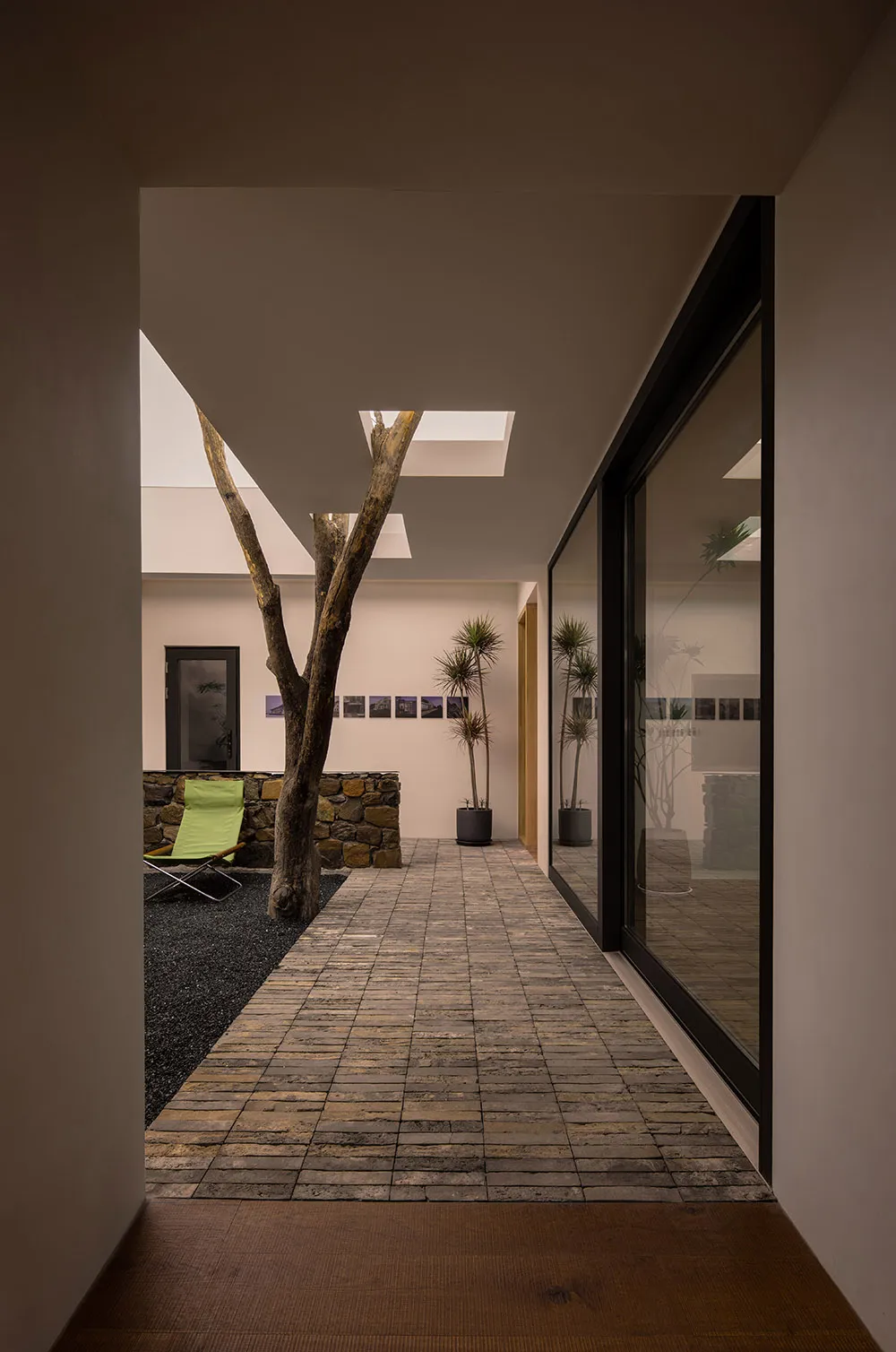 Modern residential hallway featuring brick and concrete flooring, with a central tree trunk and natural light.
