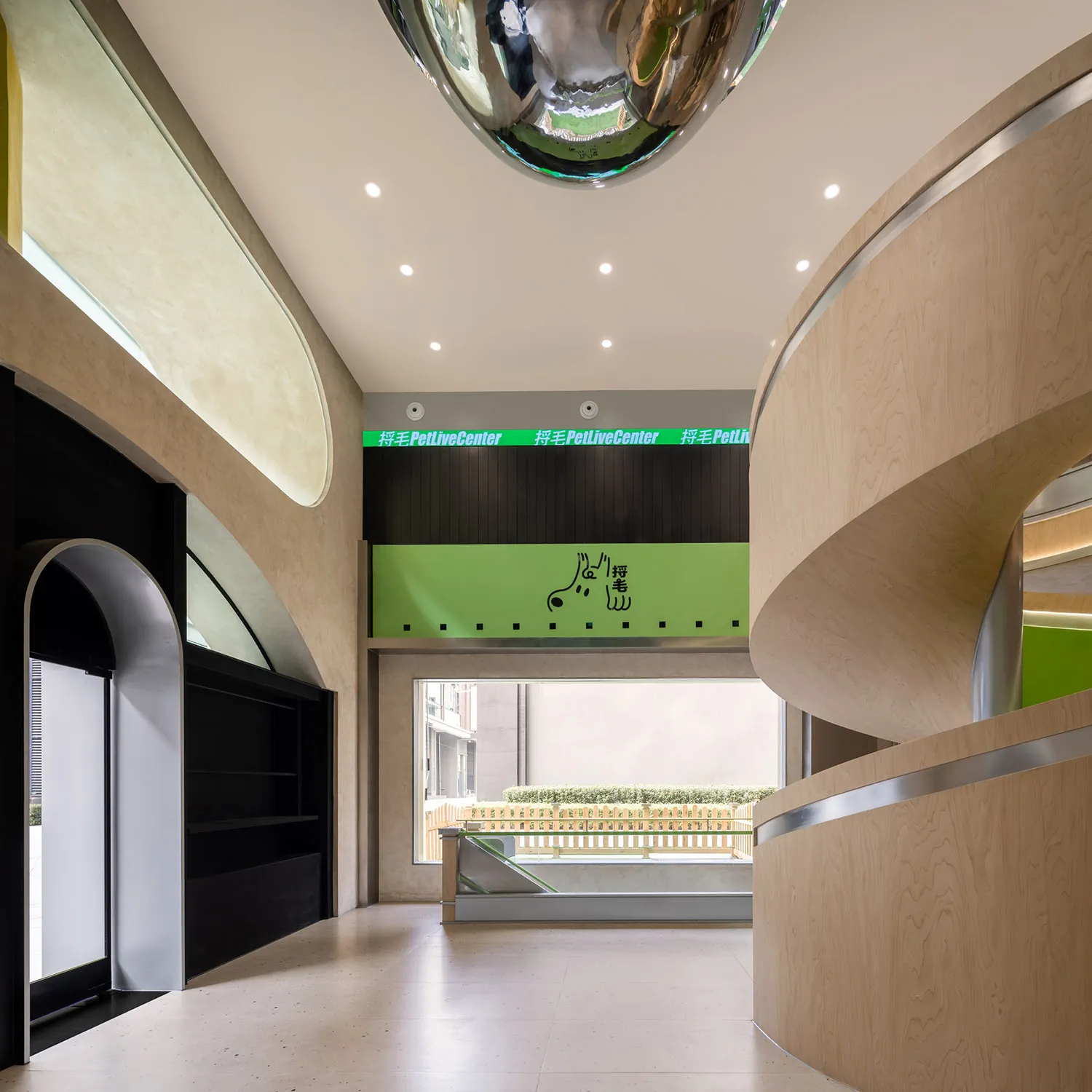 An interior of a modern urban pet living center with a sleek, curved wood reception desk and a large reflective sphere hangin