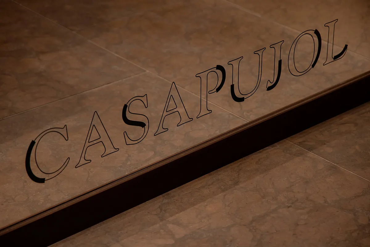 A close-up of a floor sign engraved on textured brown tiles, displaying the word 'CASAPUJOL'.