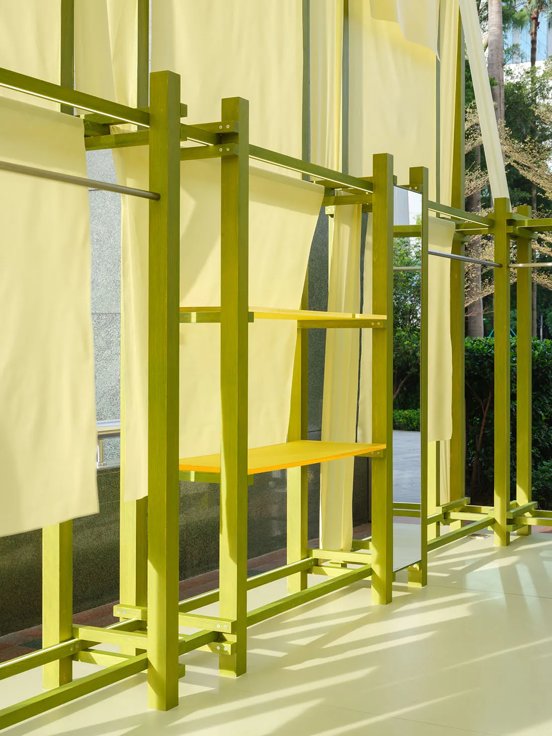 A minimalist fashion runway set featuring yellow curtains and wooden structures with integrated seating and mirrors.