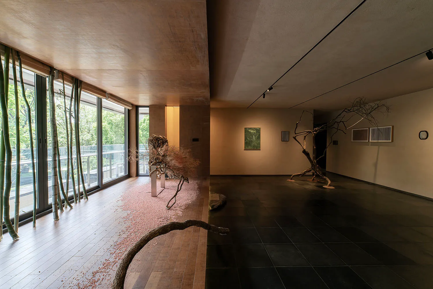 A spacious art gallery with minimalist decor featuring dry tree branches as central elements and a view of the outdoors.