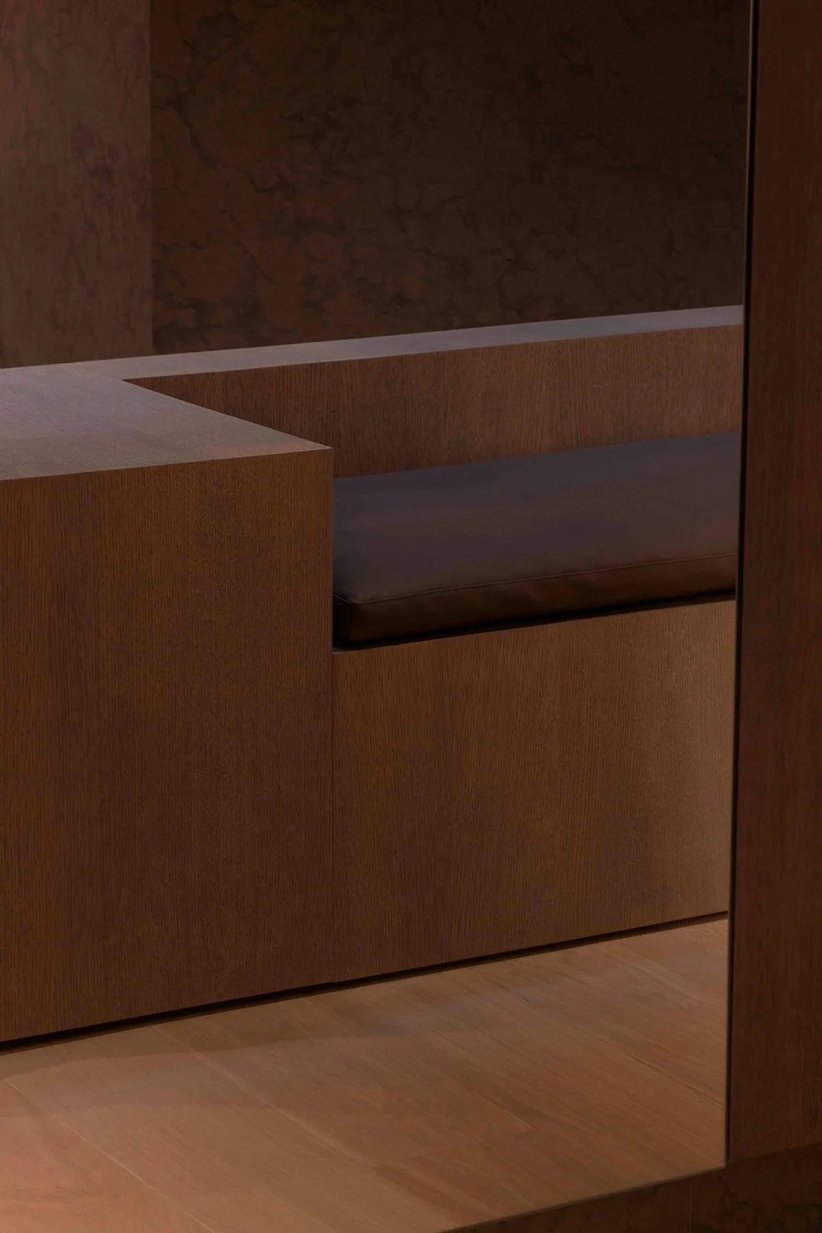 Modern interior design featuring a wooden bench with brown leather cushions and marble walls.