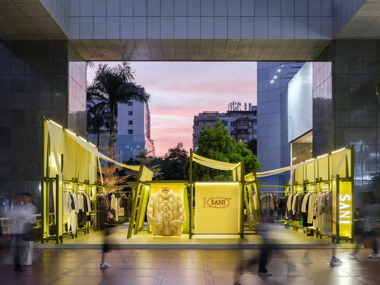 Modern retail storefront illuminated with yellow lighting features a mannequin wearing a white jacket and has a yellow banner