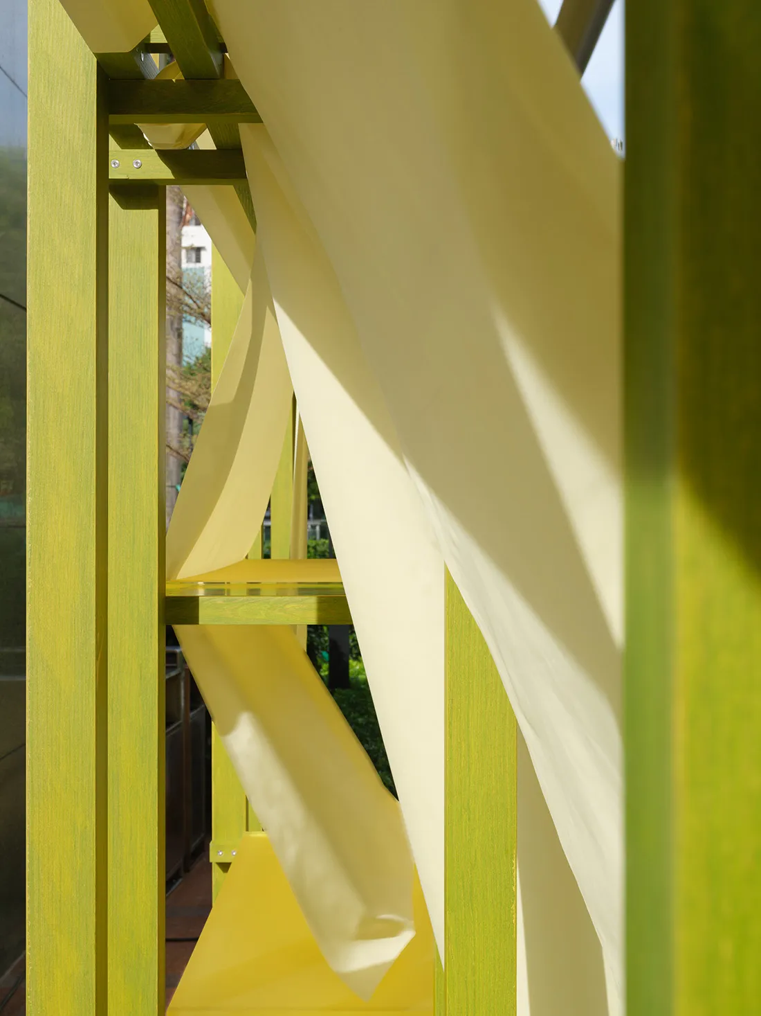 A modern architectural space featuring yellow hanging fabric and a green wooden frame.