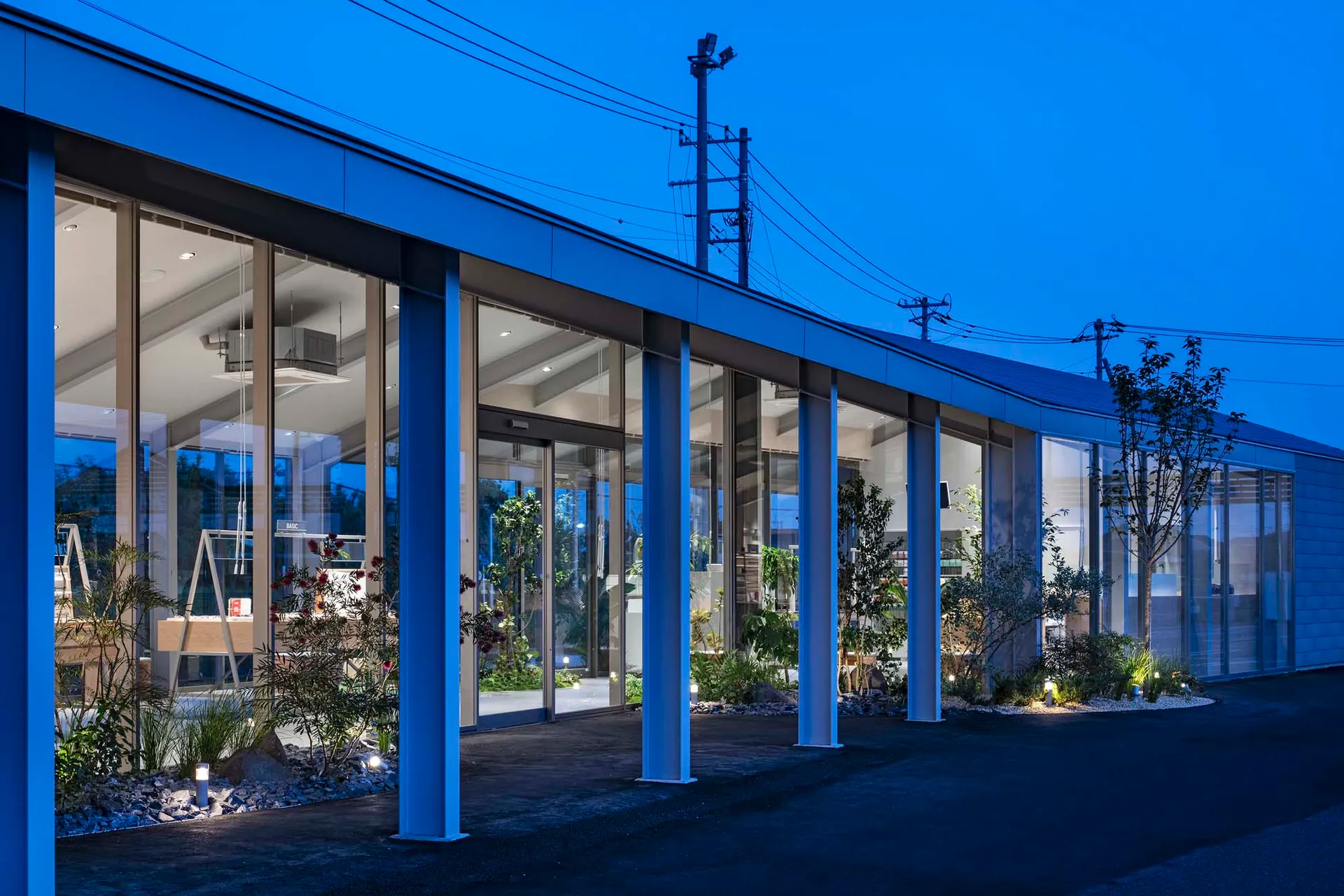 A modern building with glass walls and metal structures, viewed from the street at dusk.