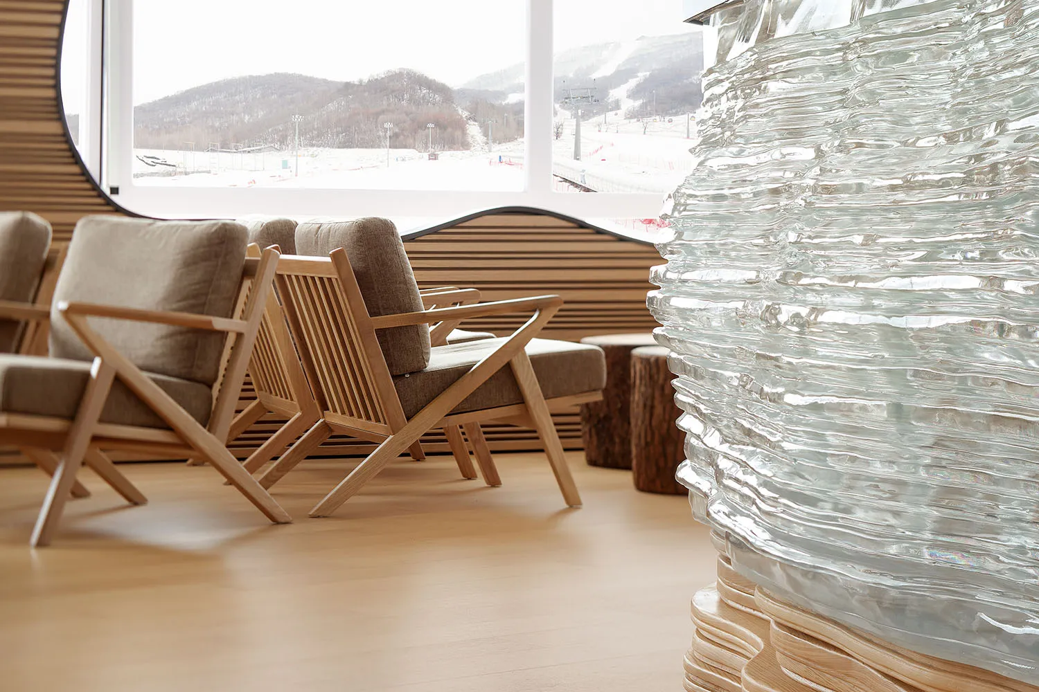 A modern living room featuring wooden furniture, a large glass window, and a textured glass sculpture.
