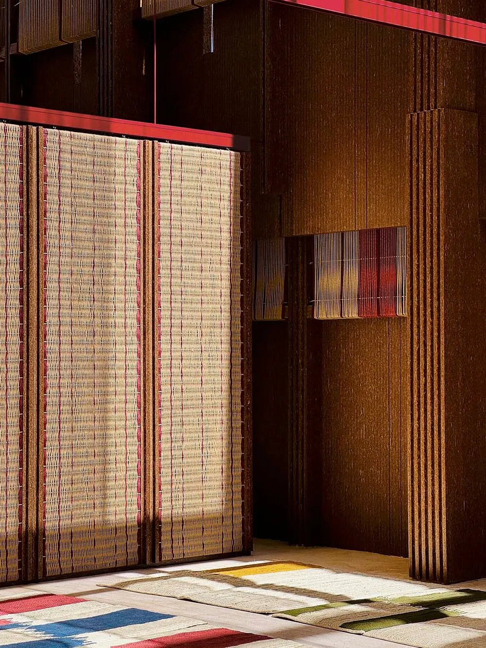 Textiles and rugs hanging on a wooden wall, showcasing various earthy and colorful patterns and textures.