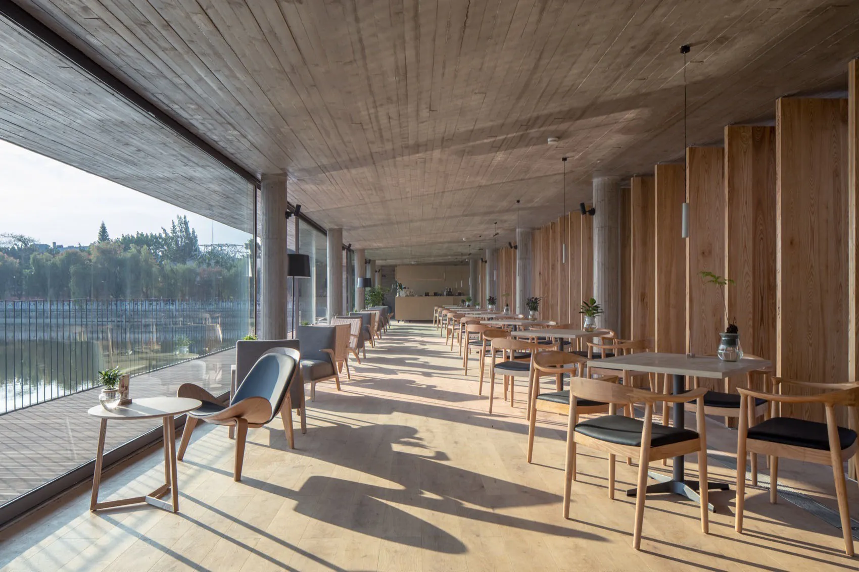 A modern cafeteria with wooden tables, chairs, and concrete ceiling and floor.