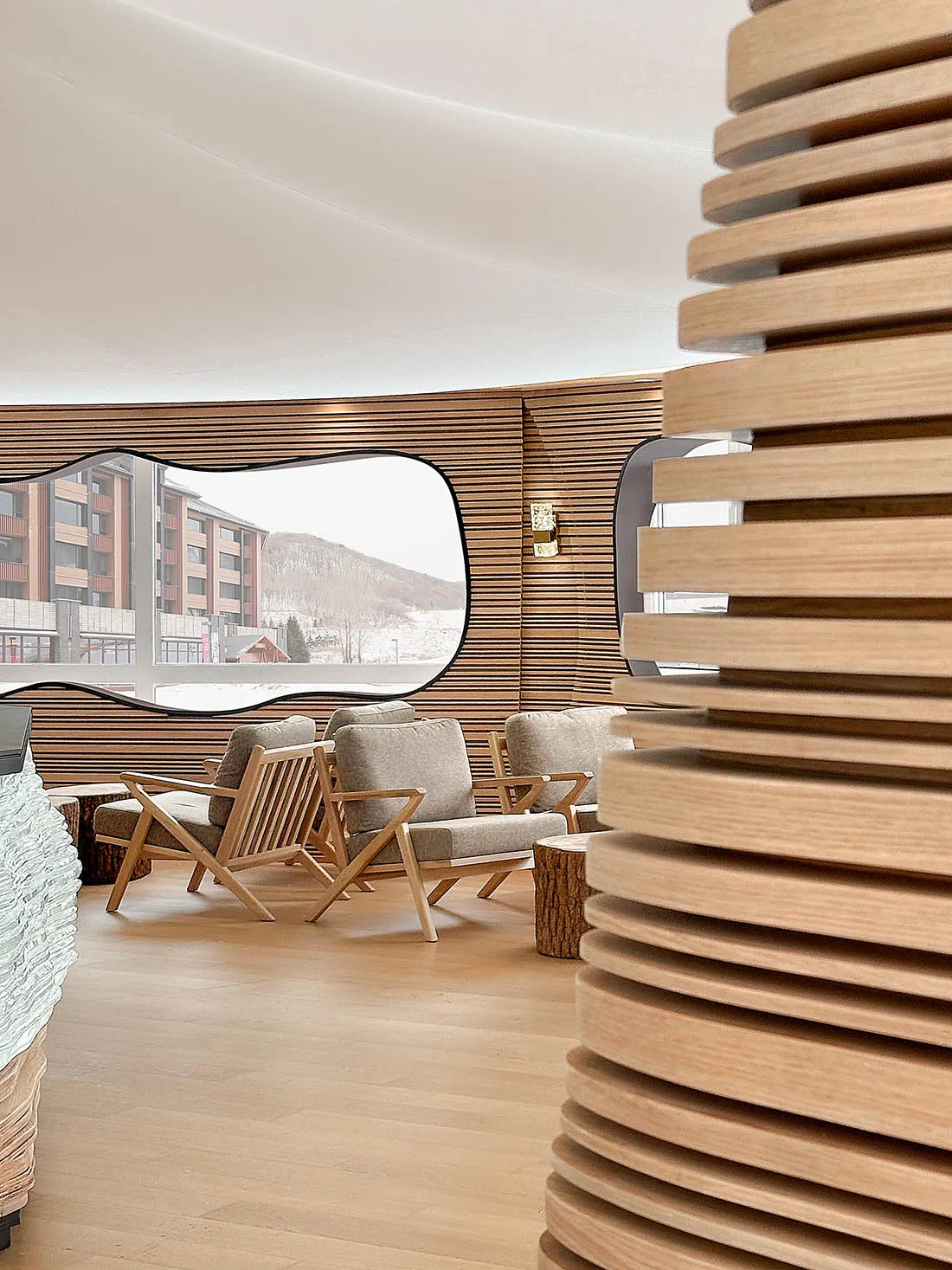 A modern hotel lobby featuring wooden walls and furniture, with a view of snowy mountains through a large window.