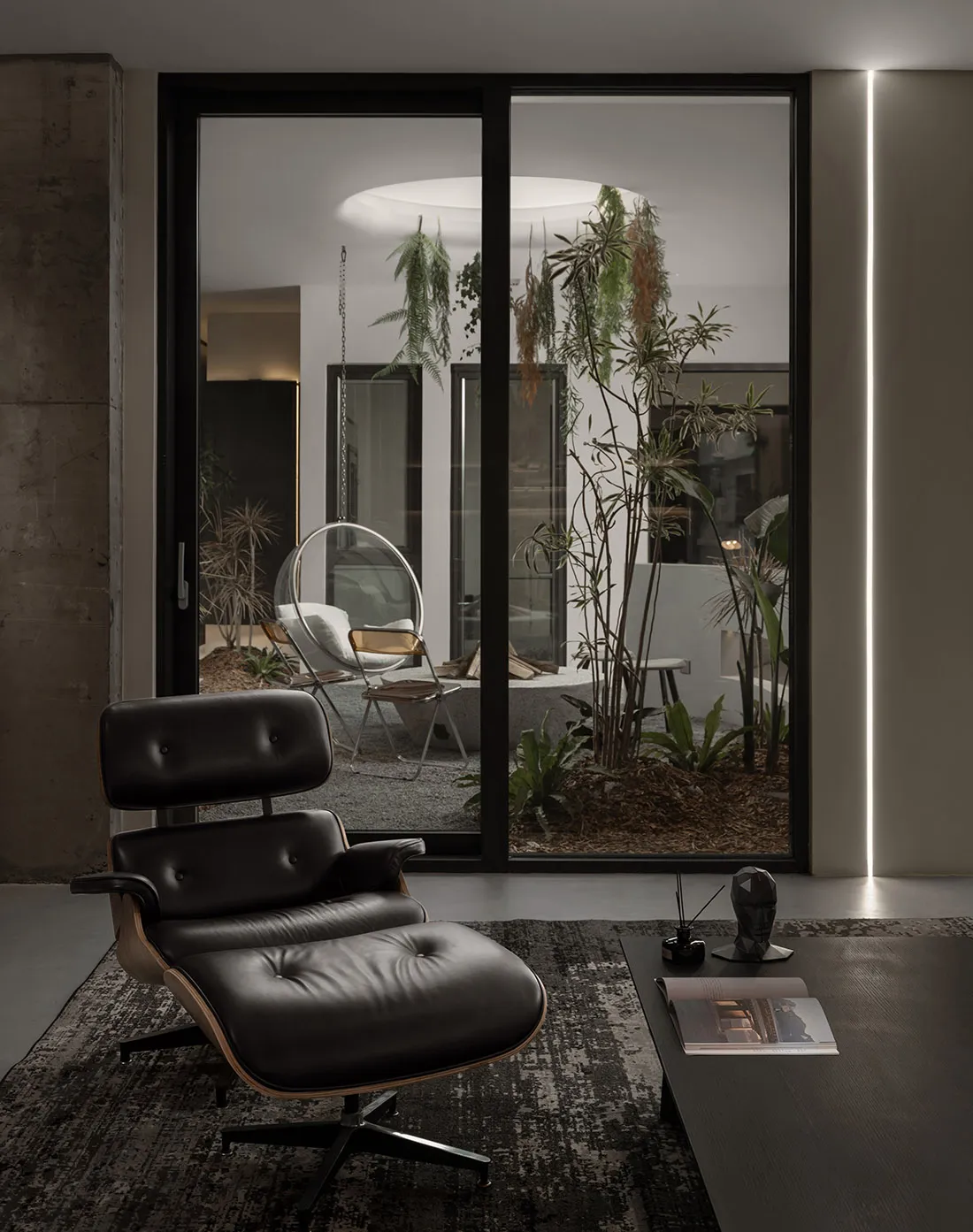 Modern living room with a black metal and leather lounge chair in front of a large window with plants.