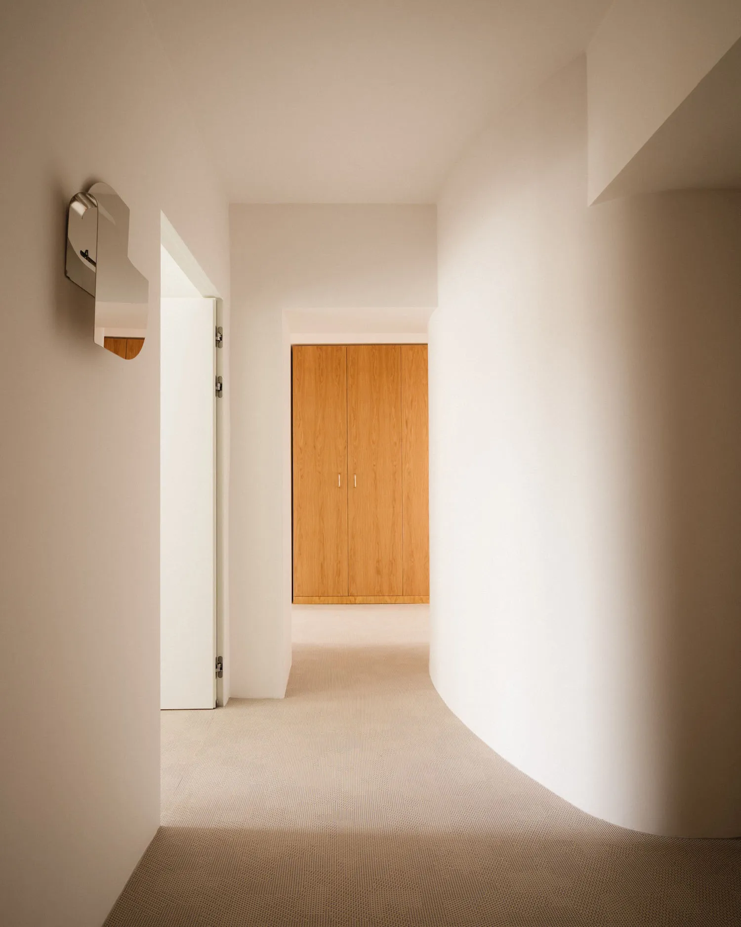 Modern minimalist hallway with concrete walls and floor, leading to a wooden closet.