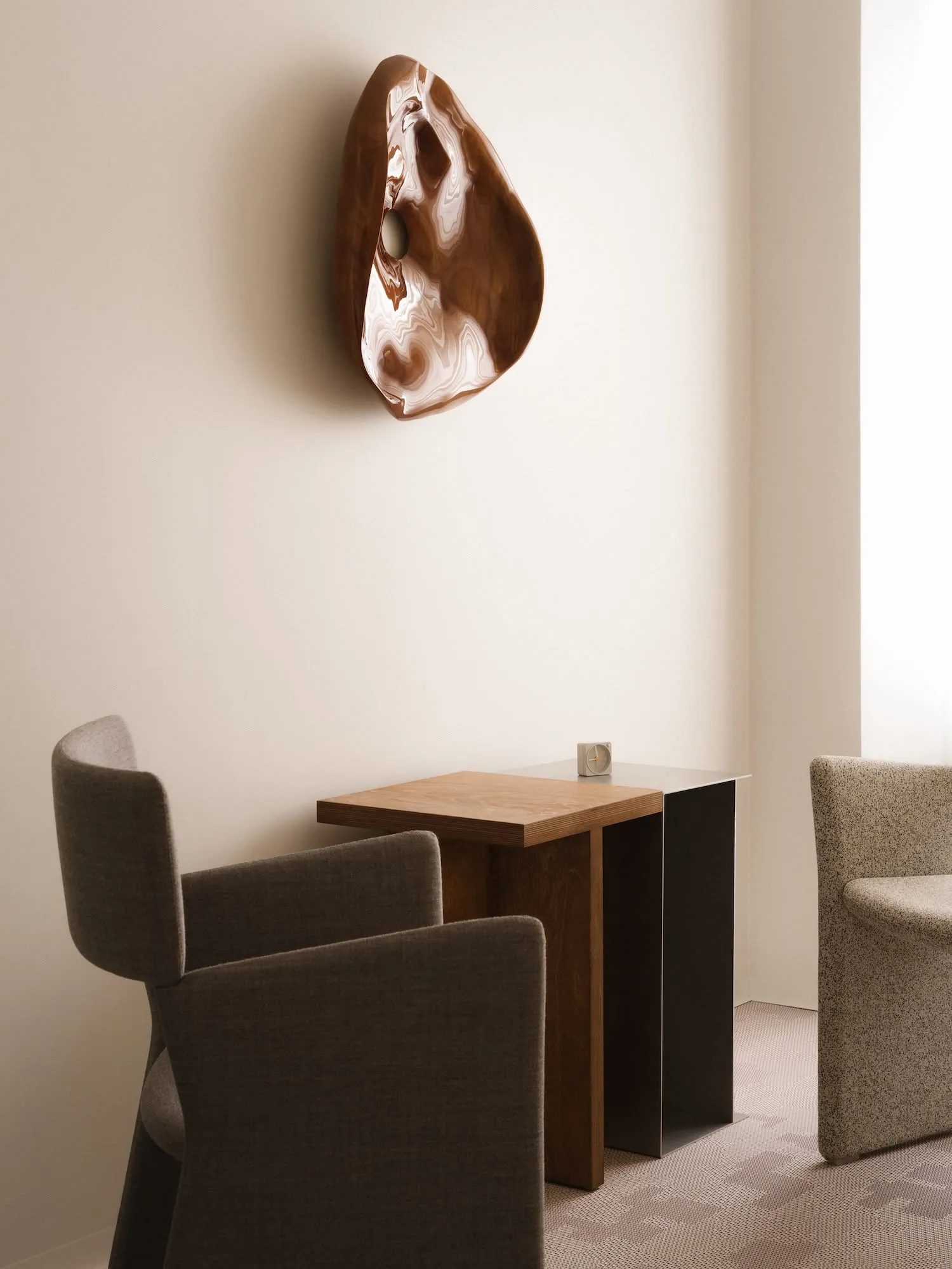 A modern interior design featuring wooden furniture with metal legs and a minimalist wall sculpture.