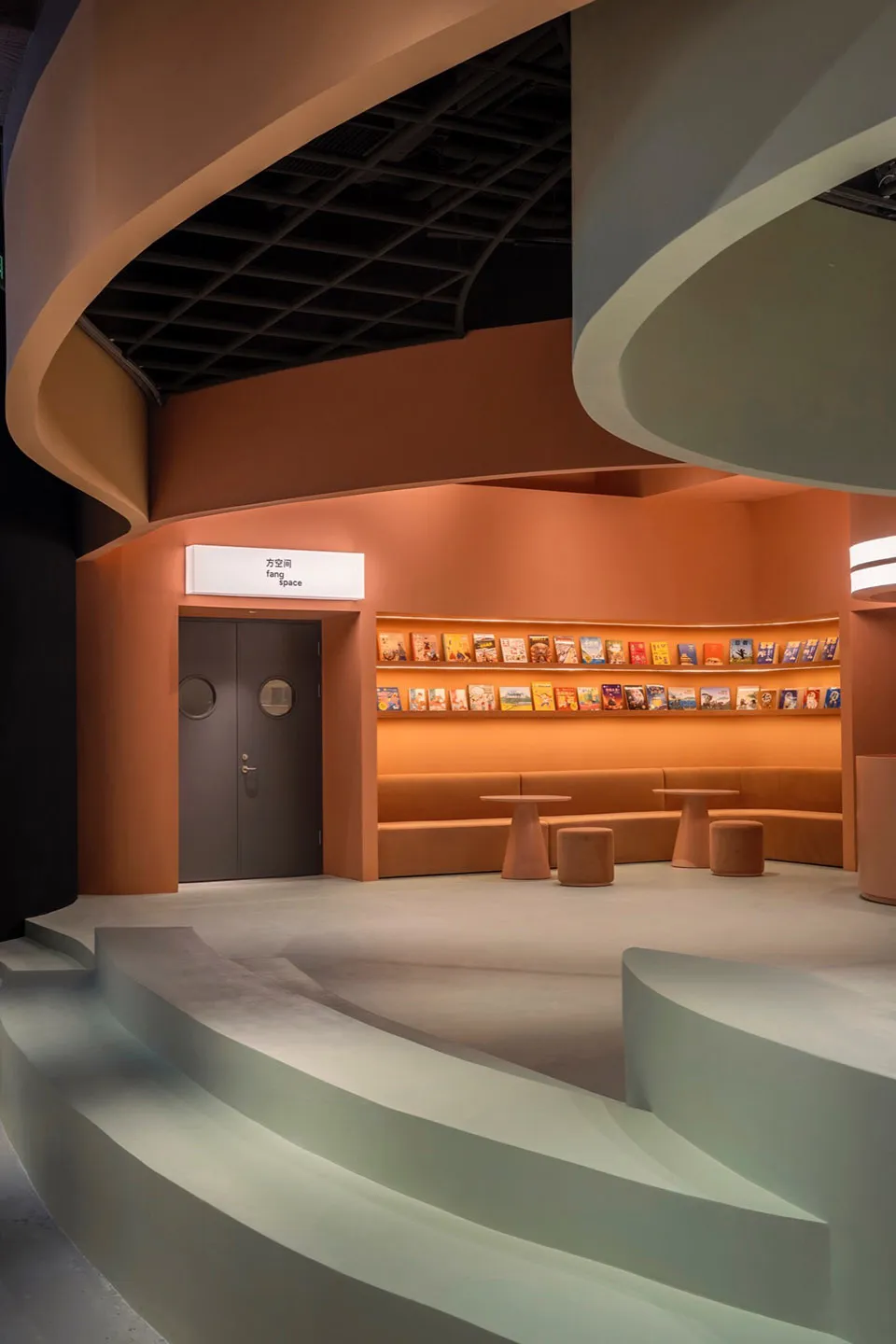 A modern library interior with concrete floors, curved walls, and a bookshelf filled with colorful books.